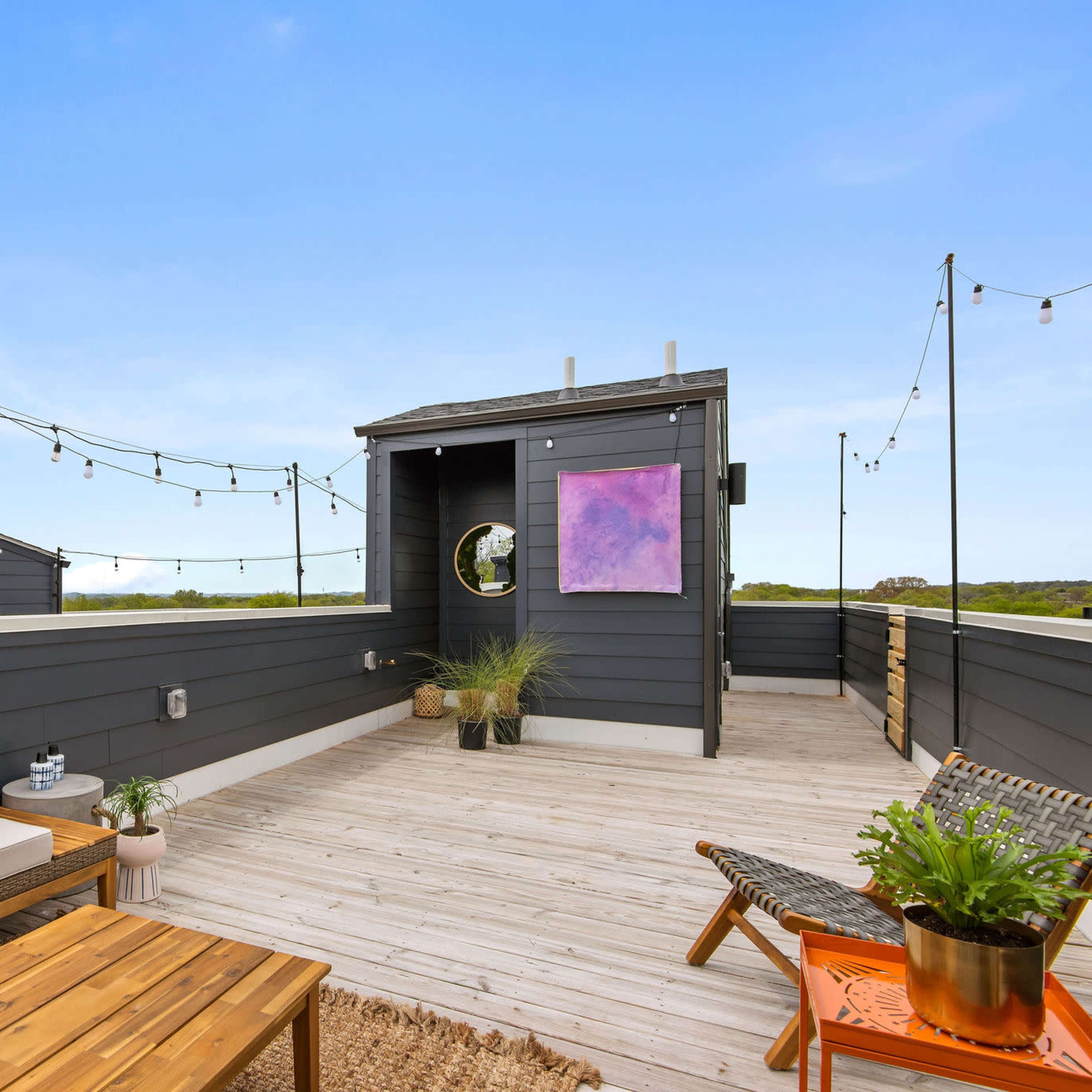 A rooftop deck features wooden furniture, string lights, and a large circular mirror on a gray wall.
