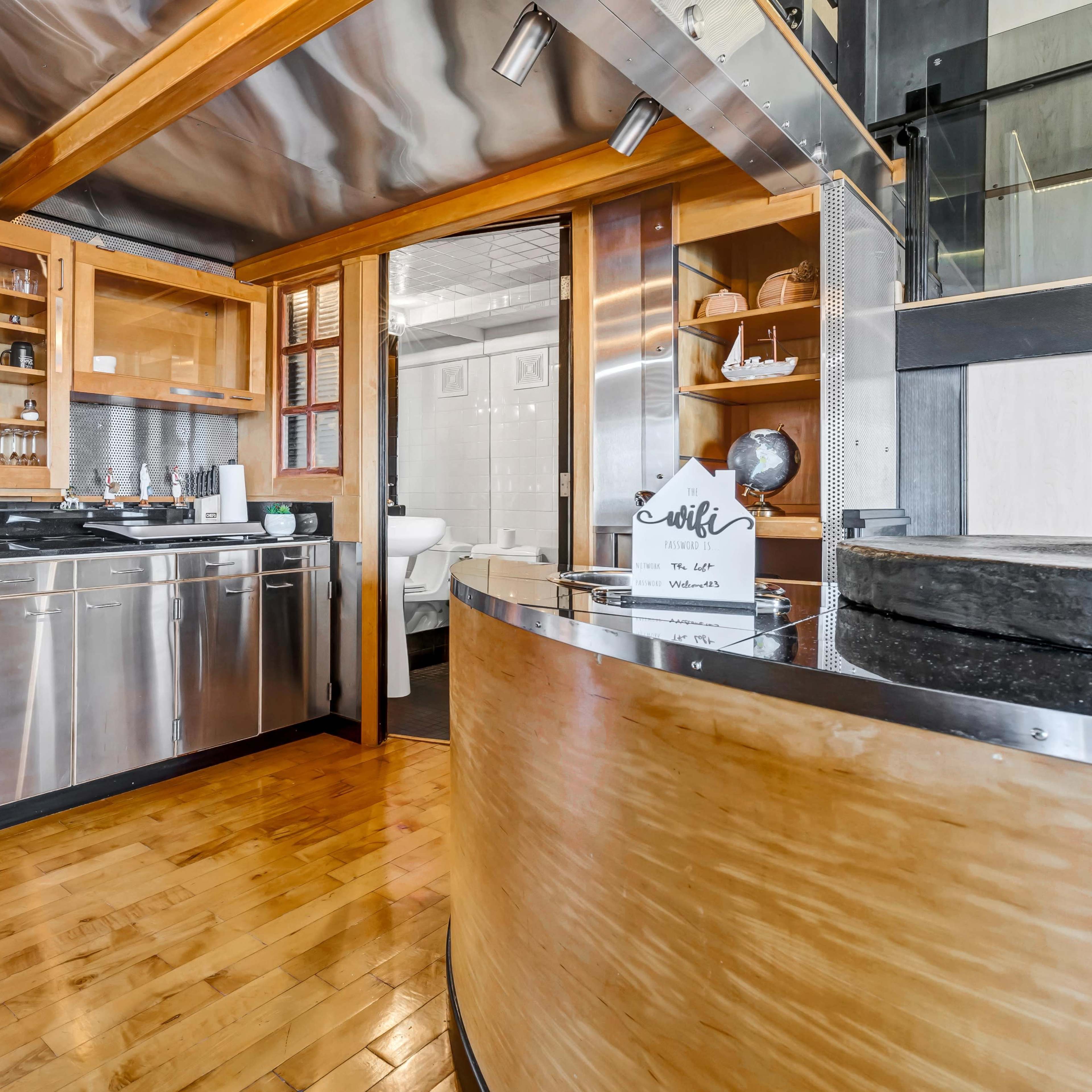 A modern kitchen with wooden cabinetry, stainless steel appliances, and an open layout connecting to another room.