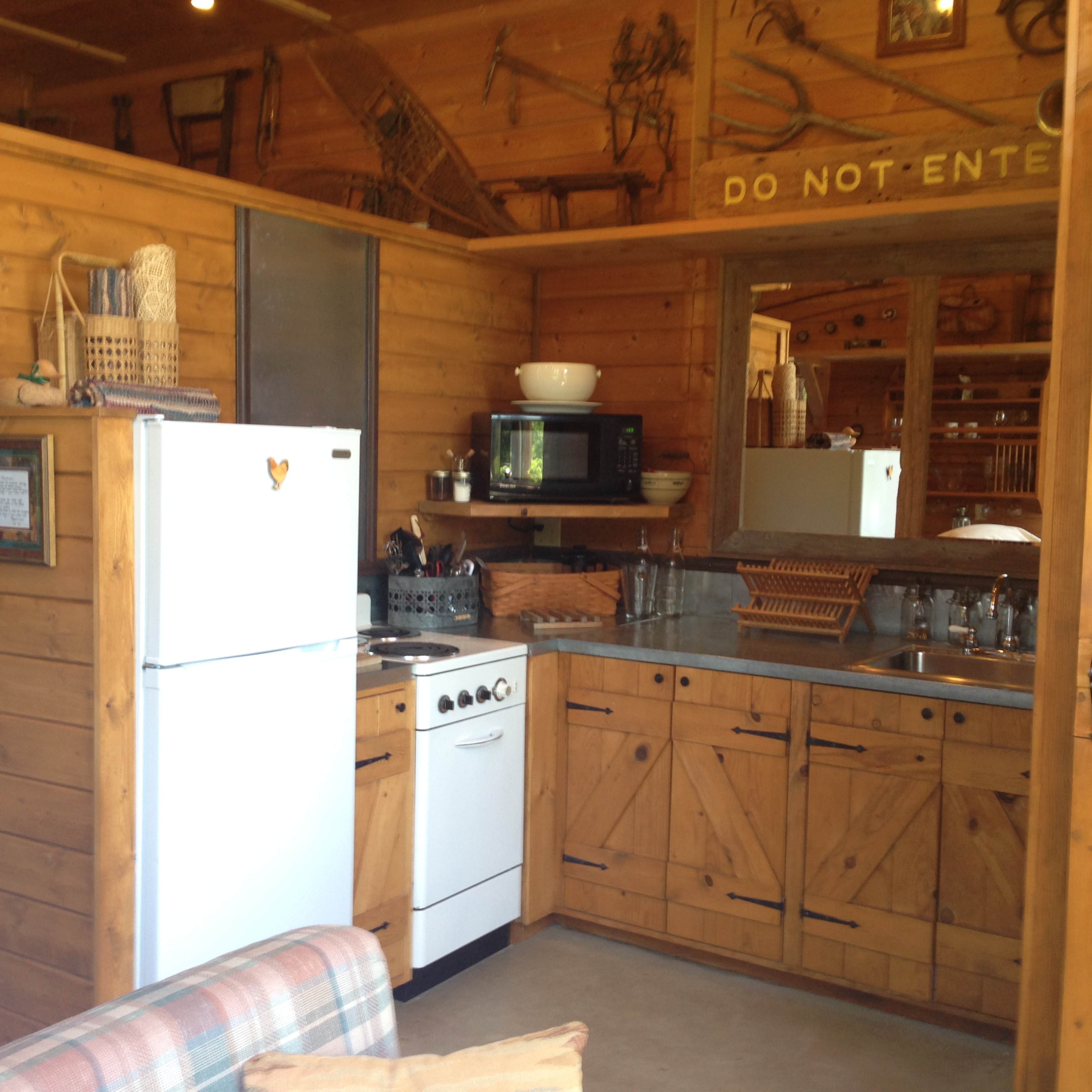 A wooden kitchen area with a refrigerator, stove, countertop, and various kitchenware neatly arranged.