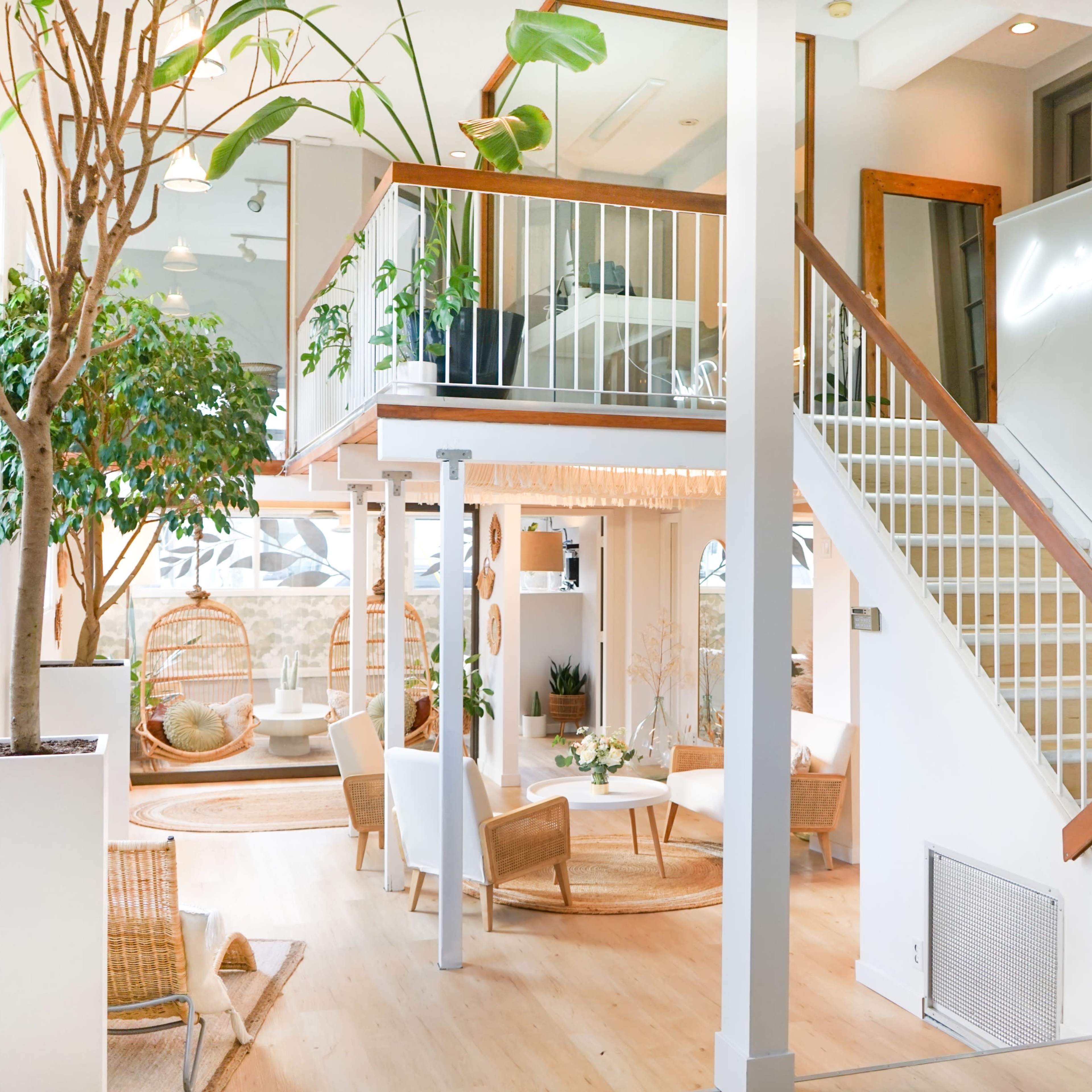 A spacious indoor area with a staircase leading to a second level, featuring plants, seating arrangements, and a well-lit ambiance.