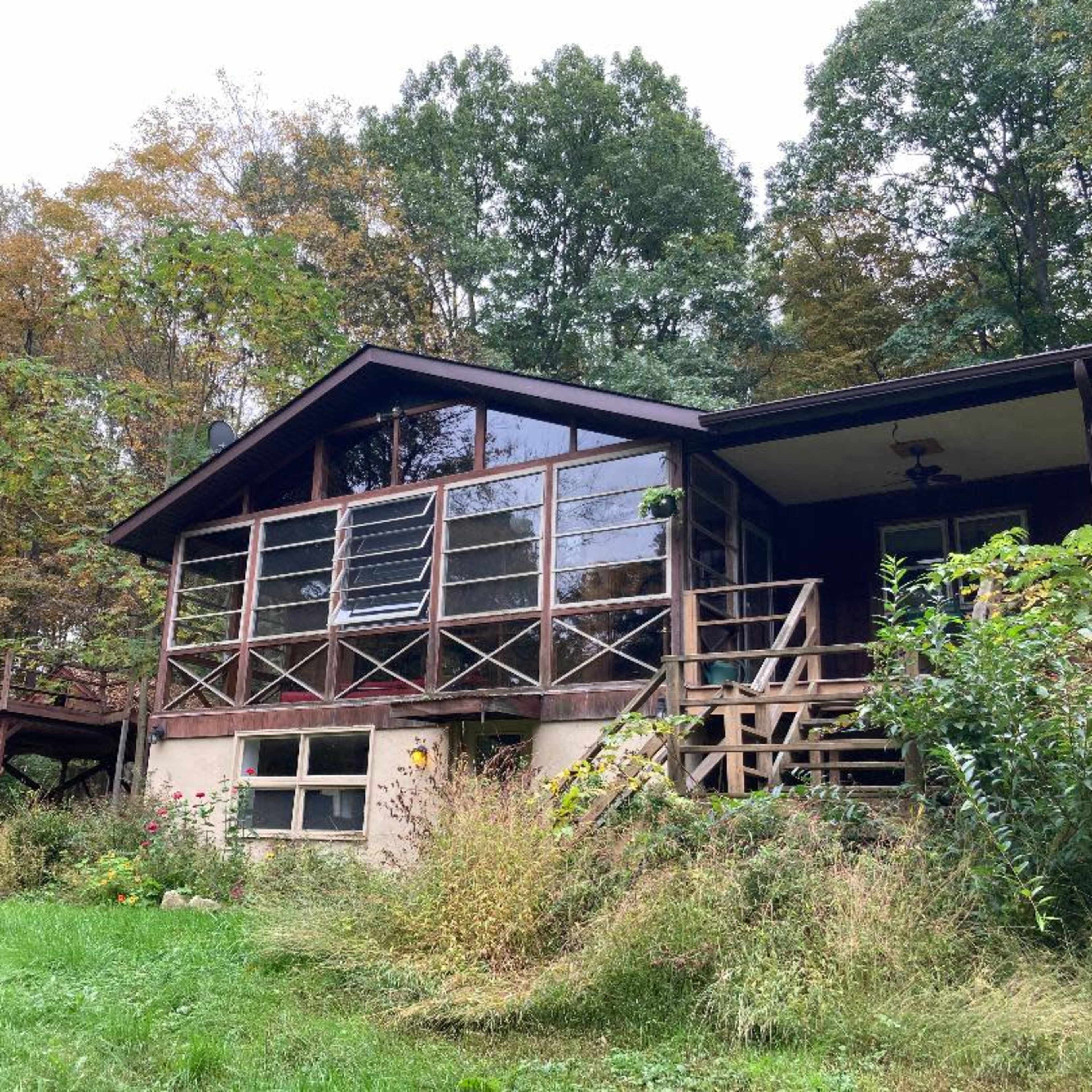 A wooden house with large glass windows is surrounded by trees and a grassy area.