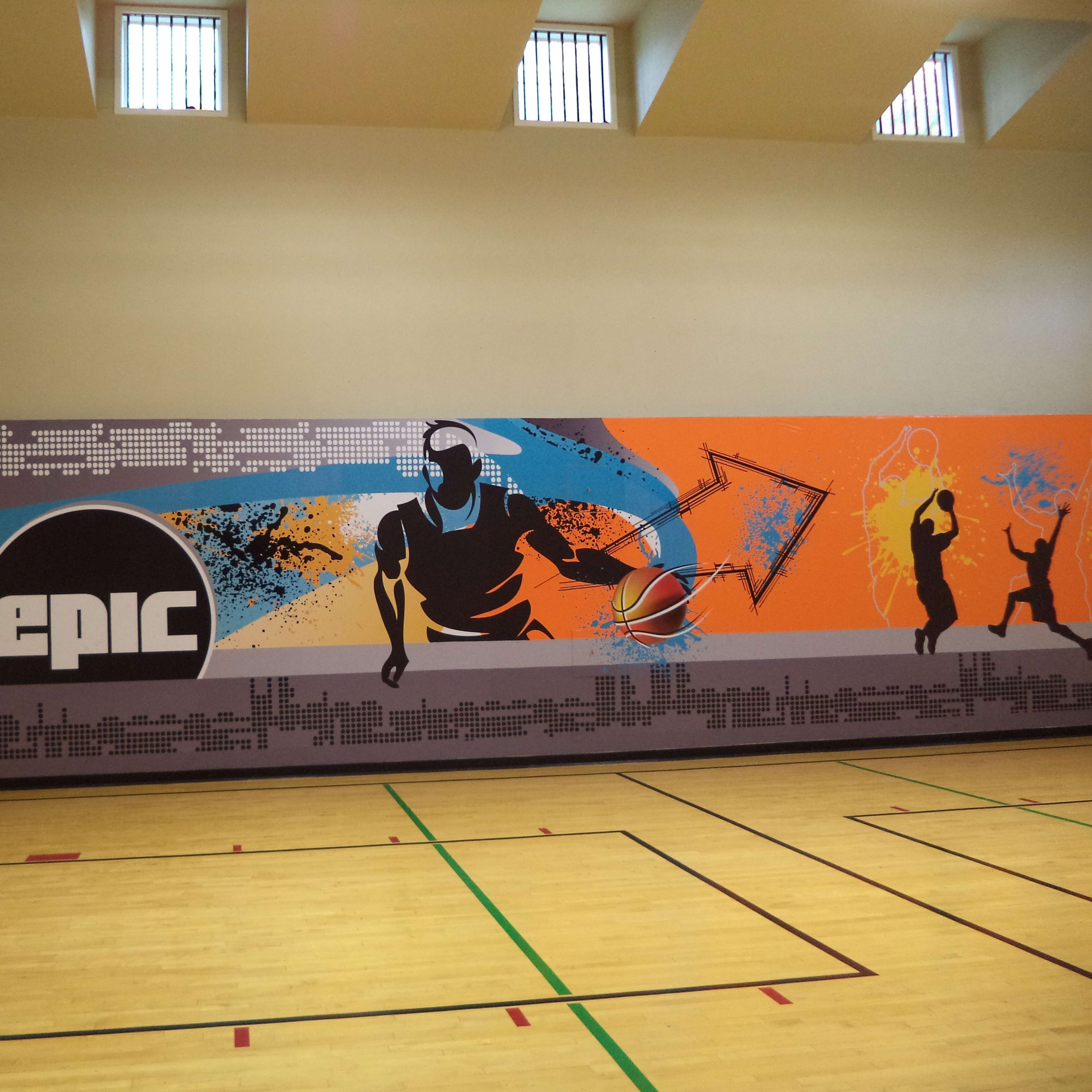 A basketball court featuring a mural with vibrant graphics of basketball players and the word "EPIC" on the wall.