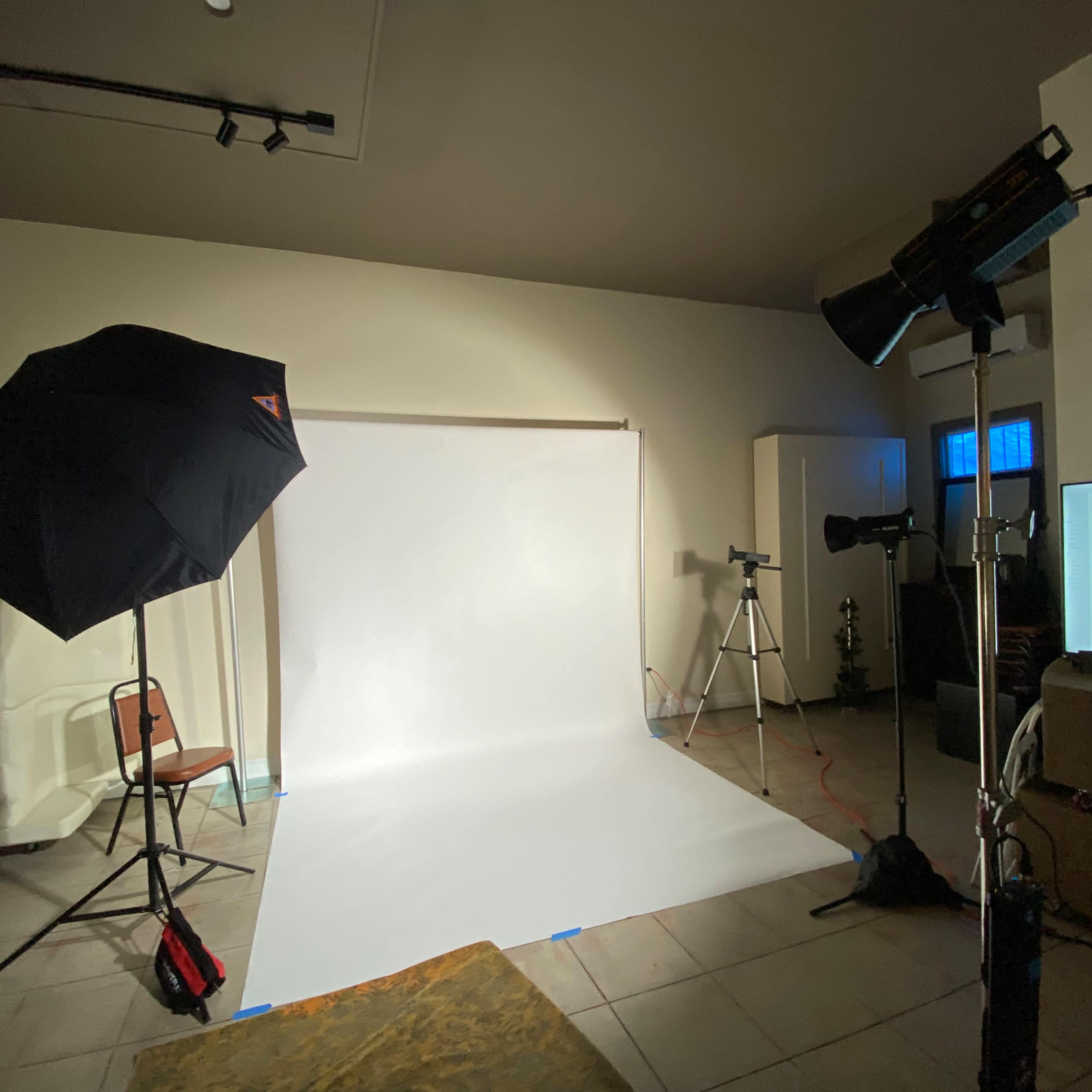 A photography studio setup featuring a white backdrop, an umbrella light, and a studio monitor.