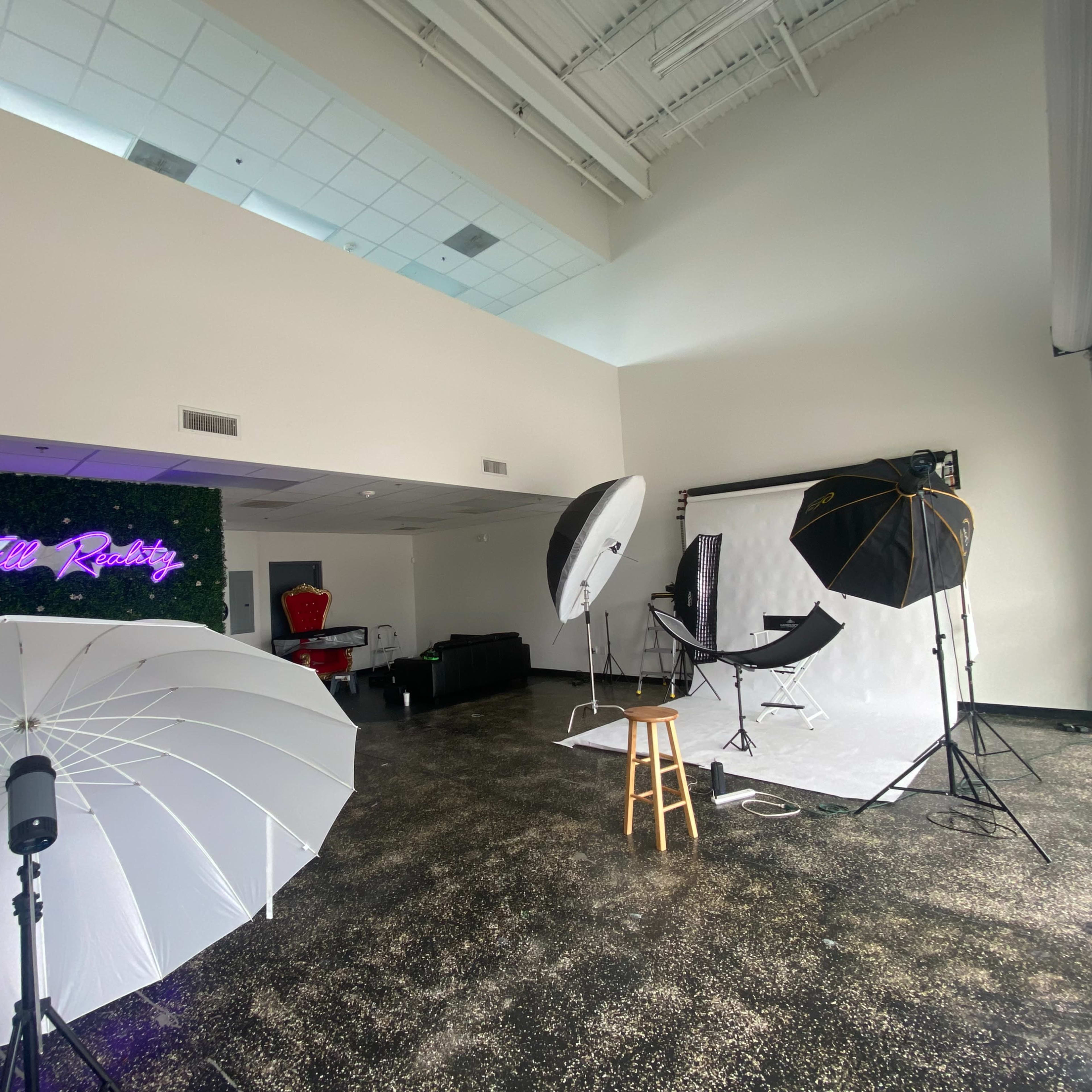A photography studio setup with lighting equipment and a backdrop, featuring a neon sign that reads "Hello Reality."