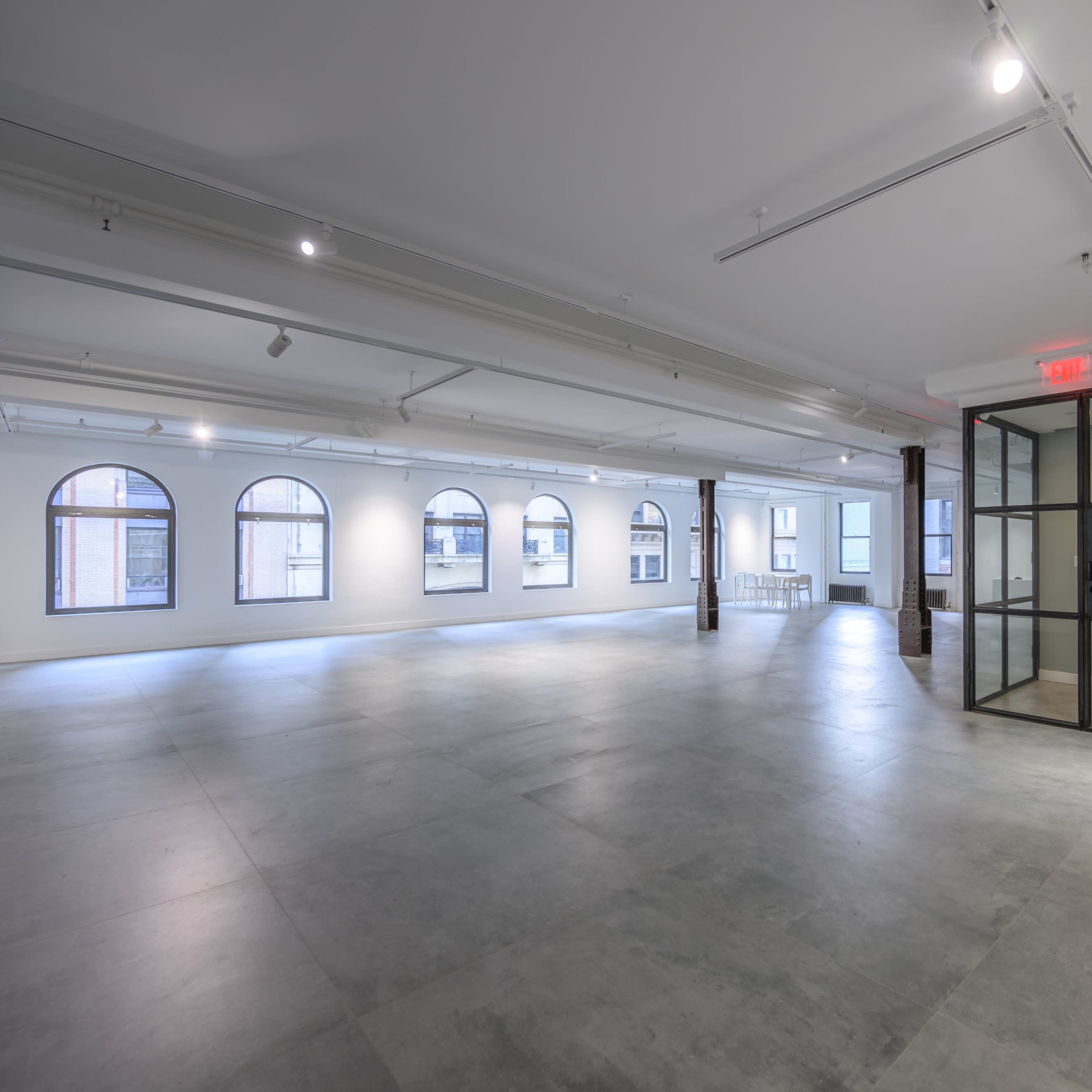 A spacious, modern interior featuring polished concrete floors, large arched windows, and a glass-walled office area.