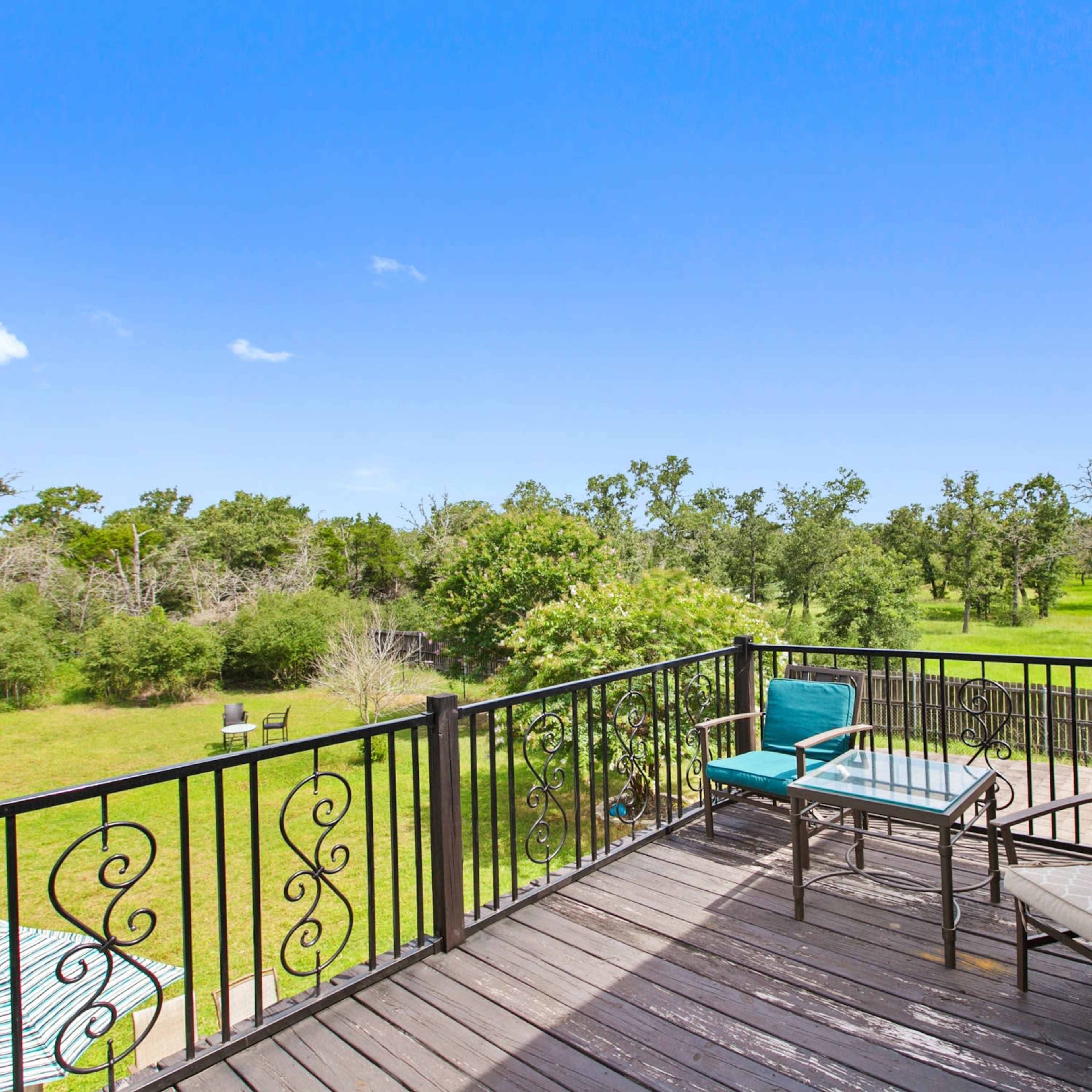 A spacious outdoor balcony with two chairs and a table, overlooking a green landscape with trees.