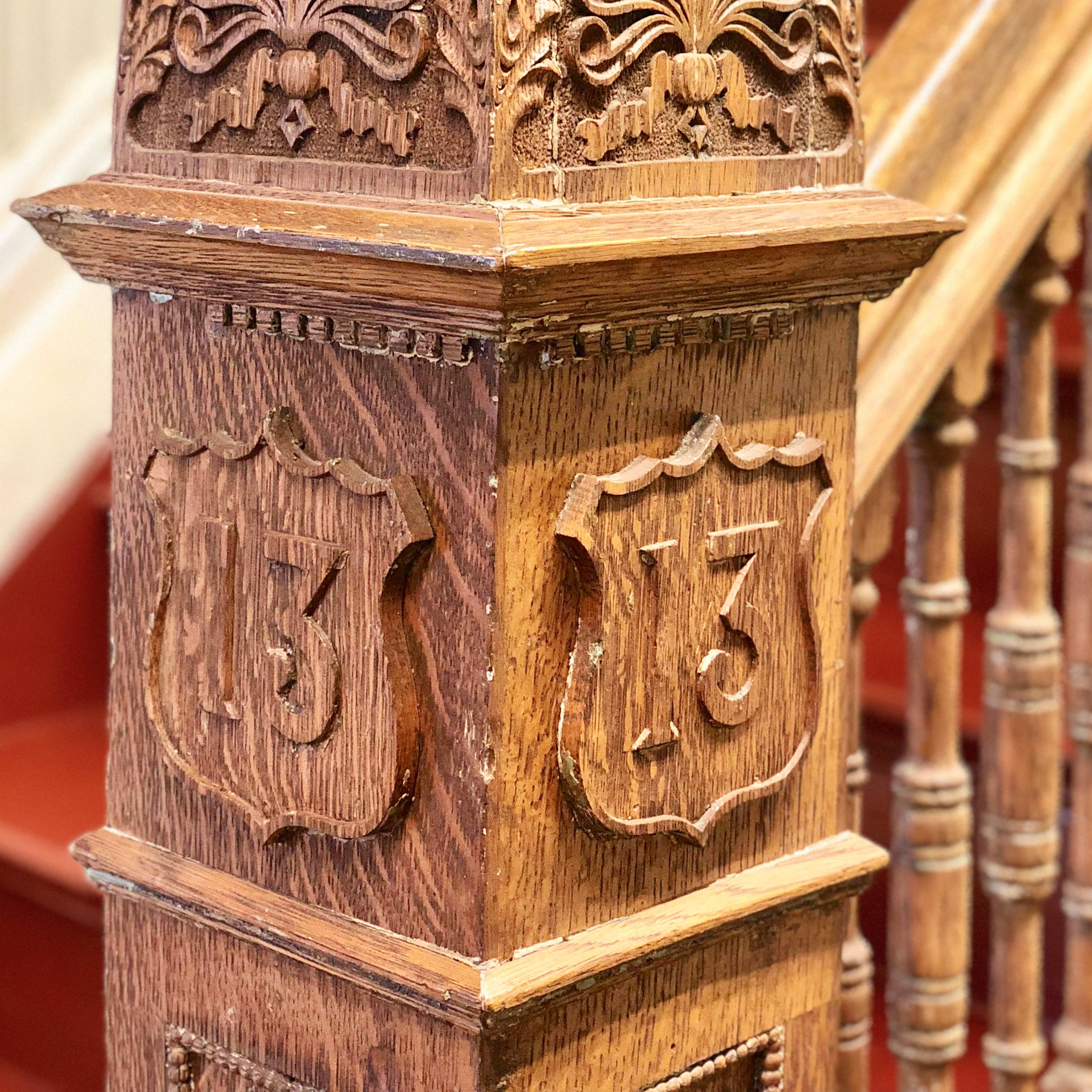 A carved wooden post with the number "13" prominently displayed on it, positioned near a staircase with red carpeting.