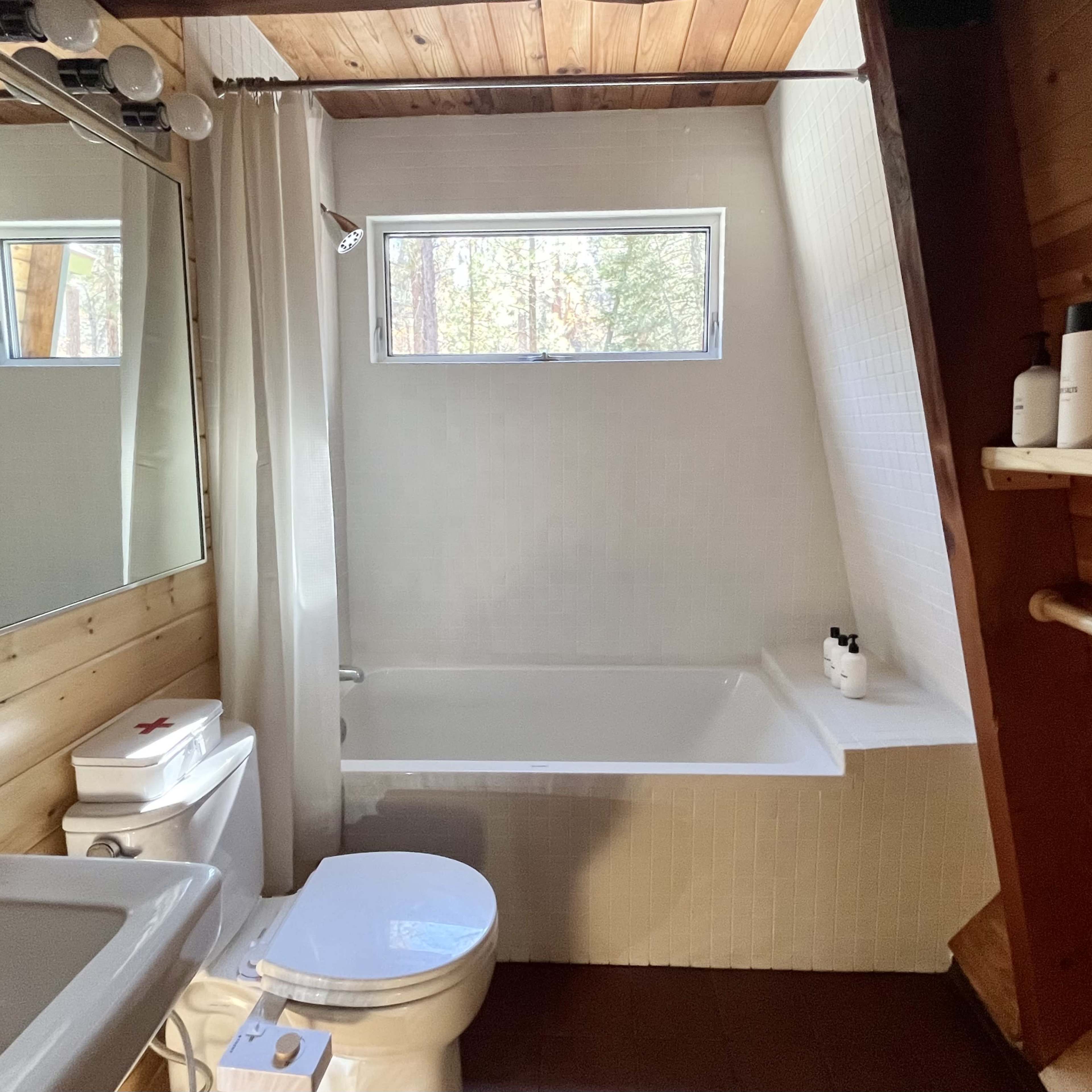 A bathroom with a bathtub, a sink, a toilet, and a window allowing light to enter.