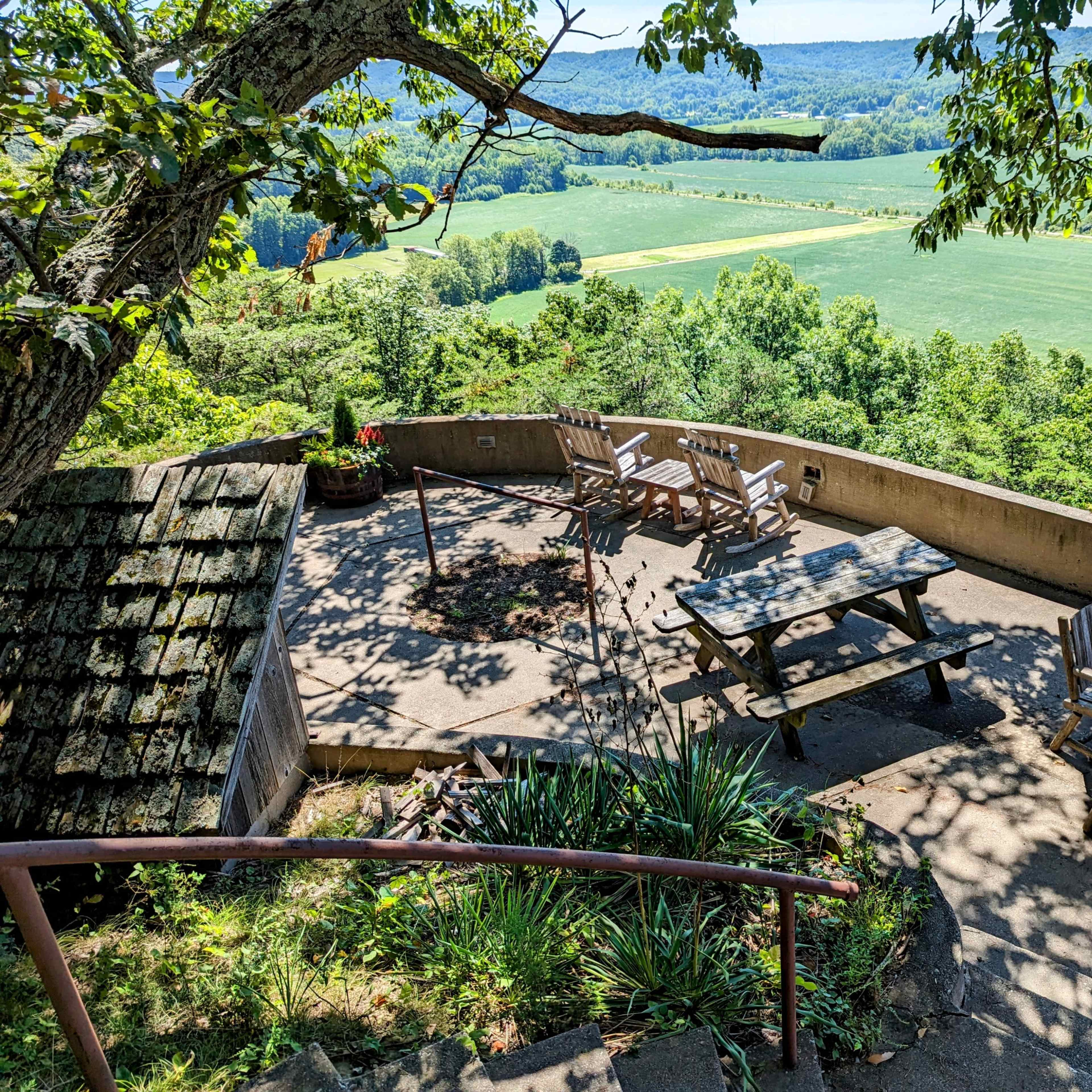 A landscaped outdoor area with seating, including chairs and tables, overlooking a green valley.