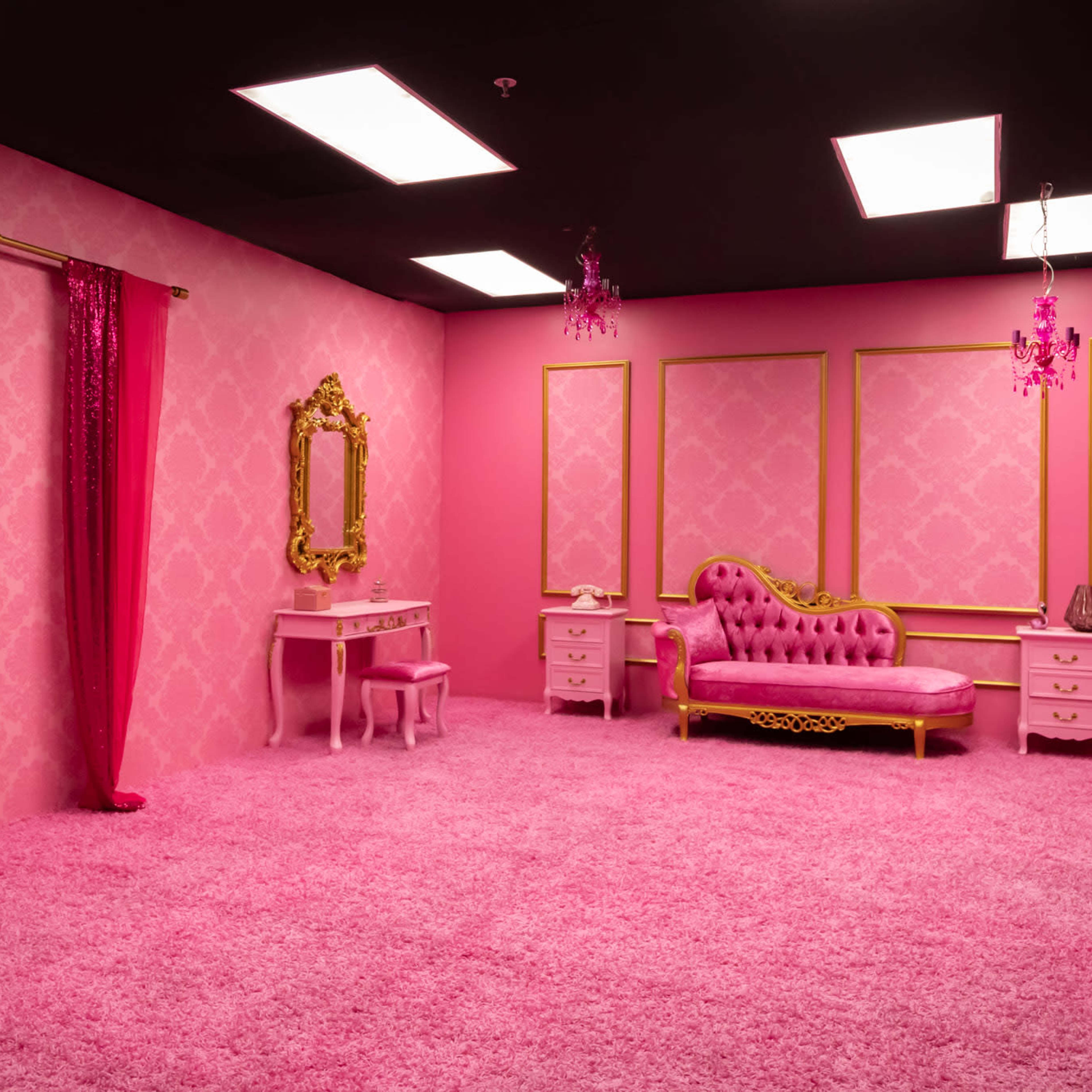 A vibrant pink room furnished with a plush pink chaise lounge, a small vanity table, and a mirror, all set against pink walls and carpeting.