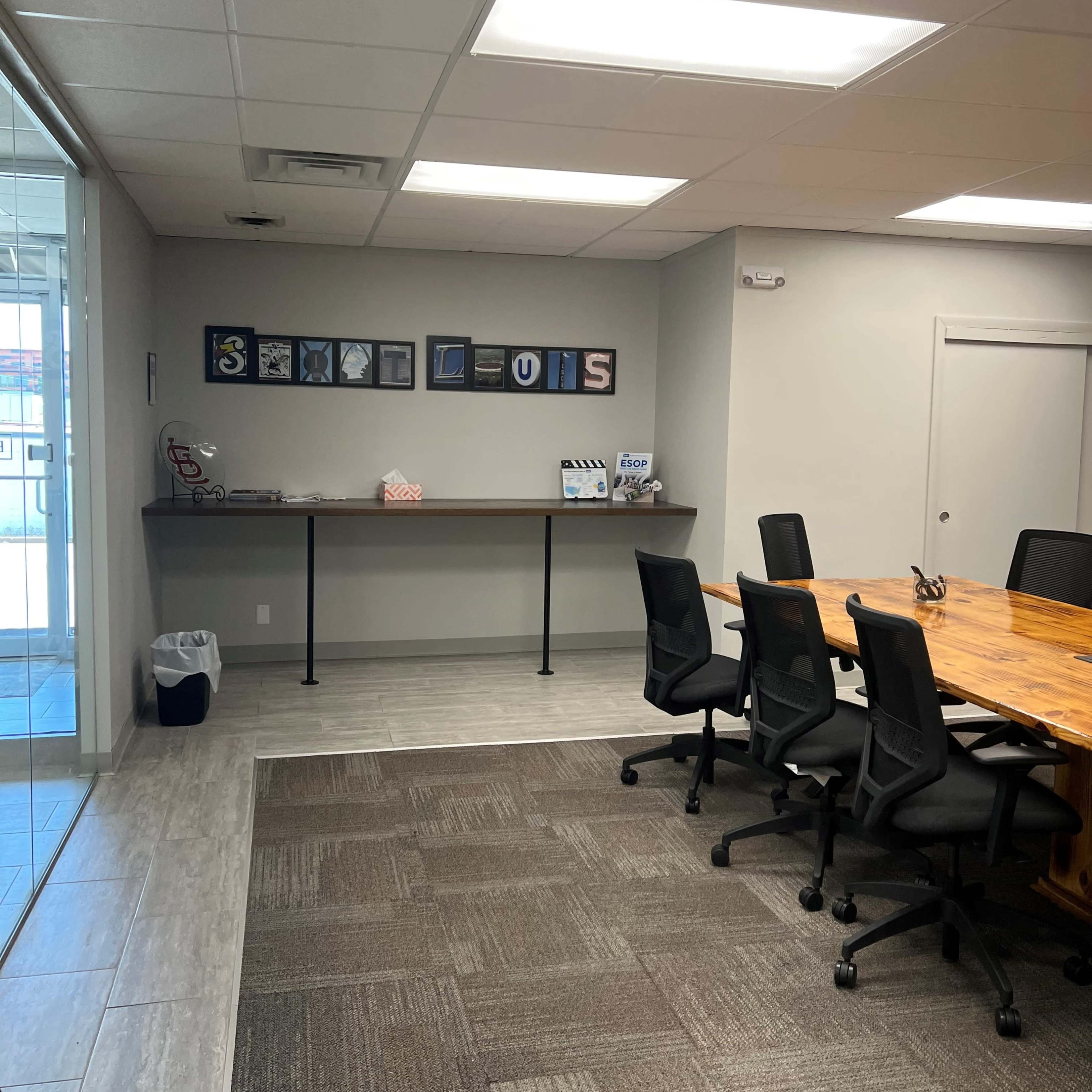A modern conference room features a long table surrounded by black chairs, with a display of framed letters on the wall spelling "ST. LOUIS."
