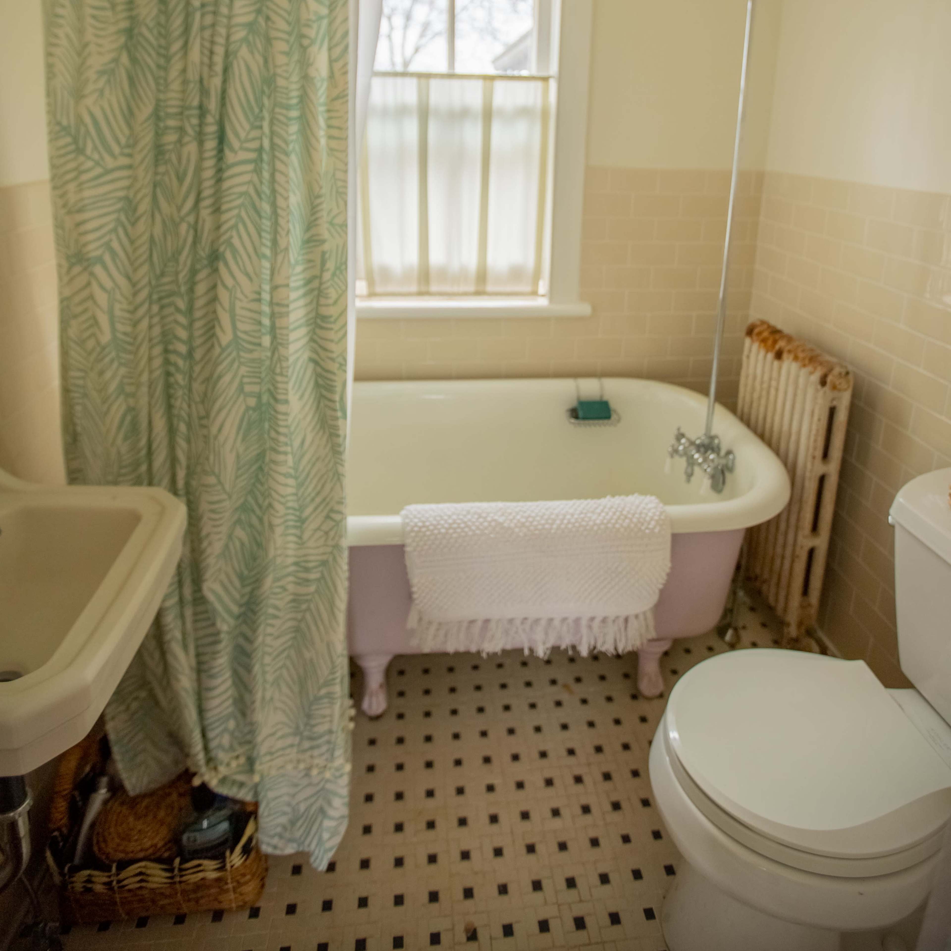The bathroom features a clawfoot bathtub, a shower with a curtain, a toilet, and a sink, all set against neutral wall tiles and large windows.