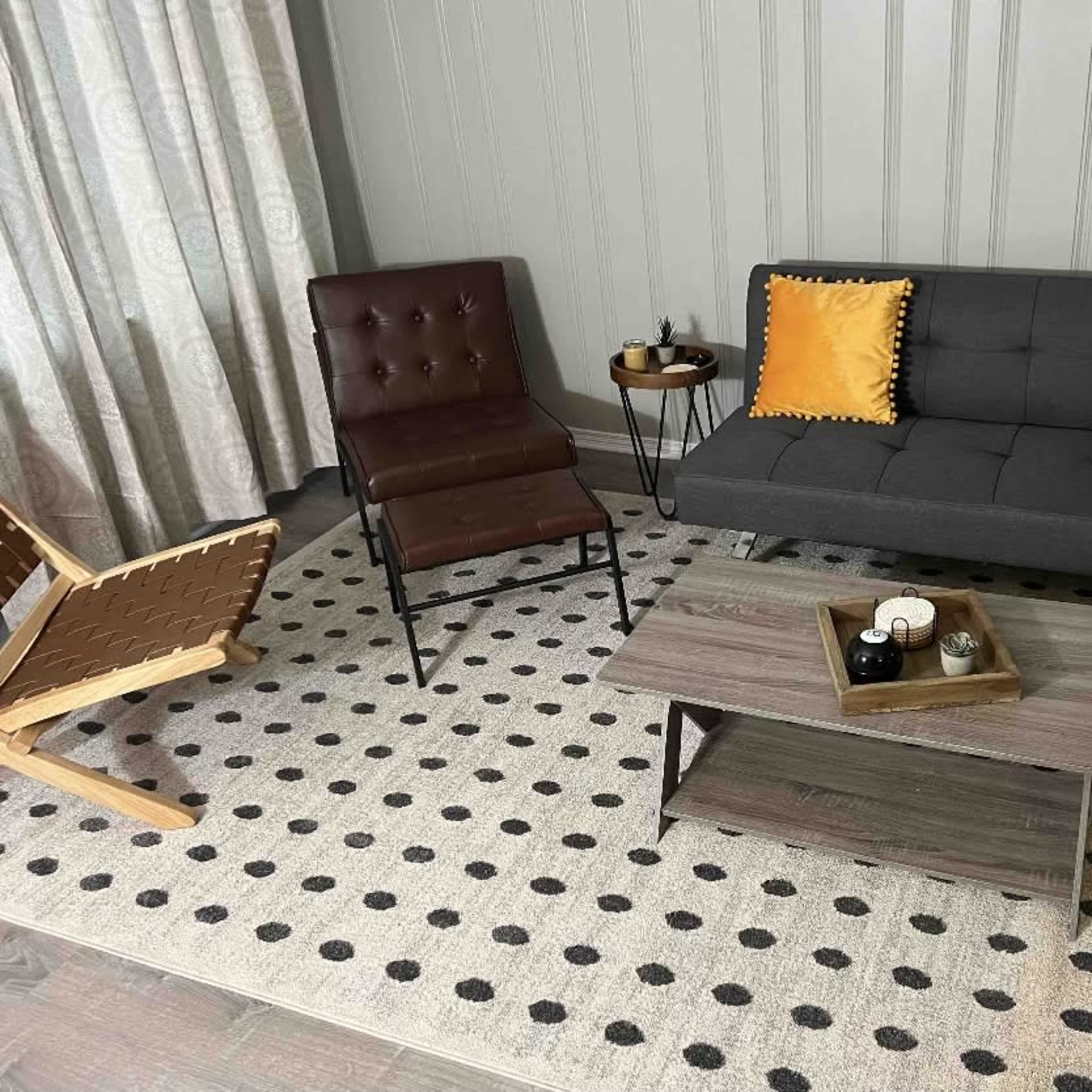 A modern living room setup with a gray sofa, a brown chair, a round side table, and a patterned area rug.