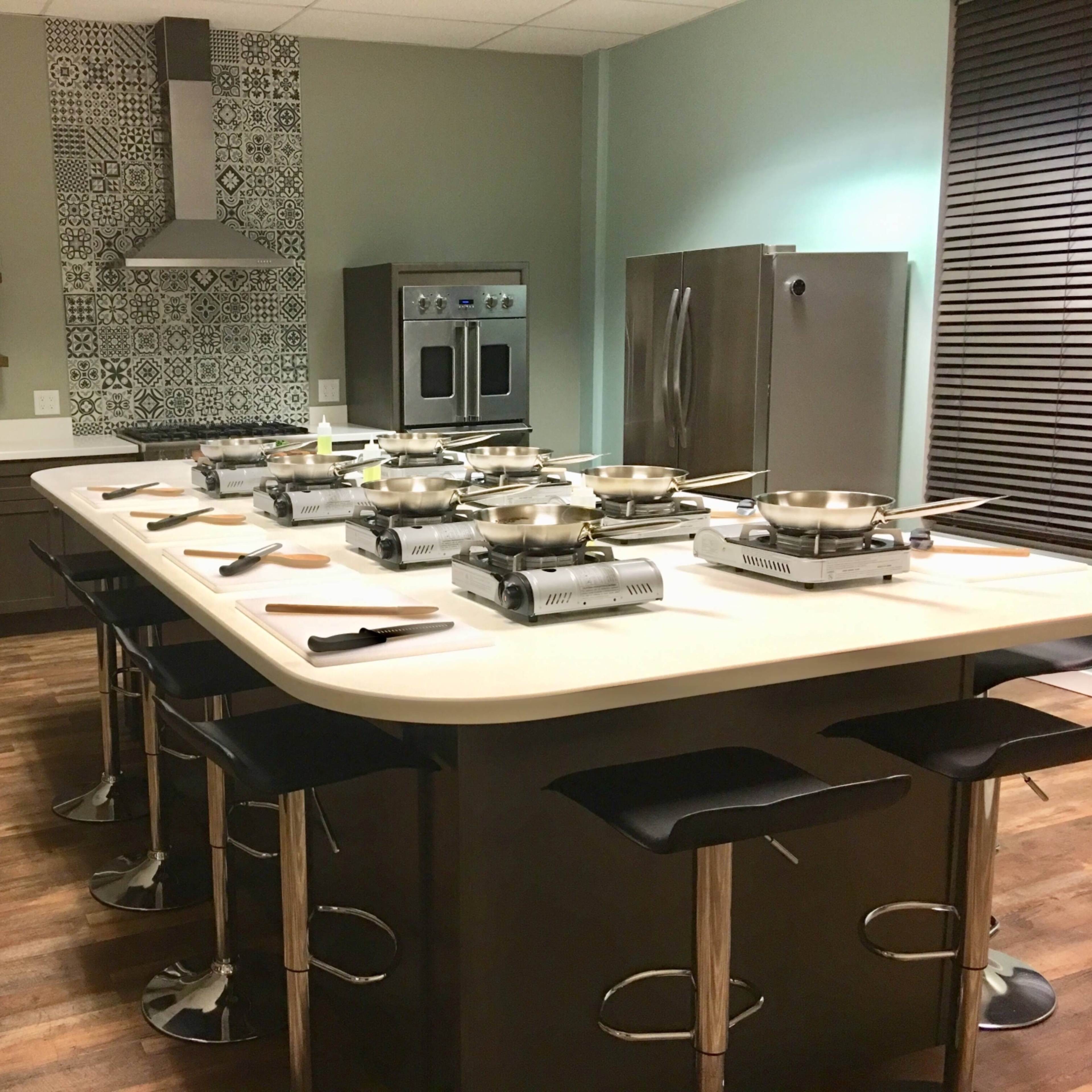 A modern kitchen space with a large island, multiple cooking stations, stainless steel appliances, and a patterned backsplash.
