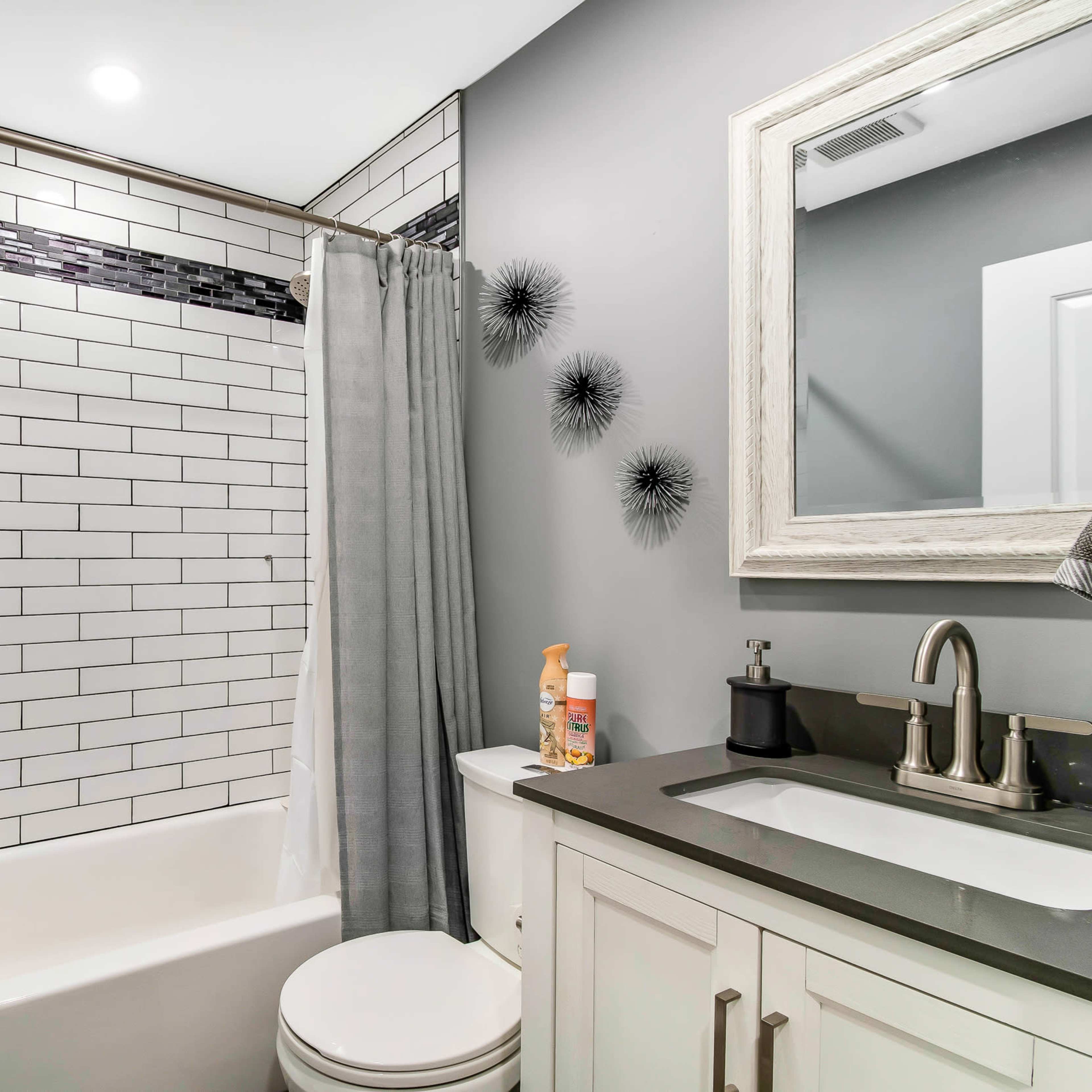 A modern bathroom featuring a bathtub with a tiled wall, a shower curtain, a mirror, and a sink with a countertop.