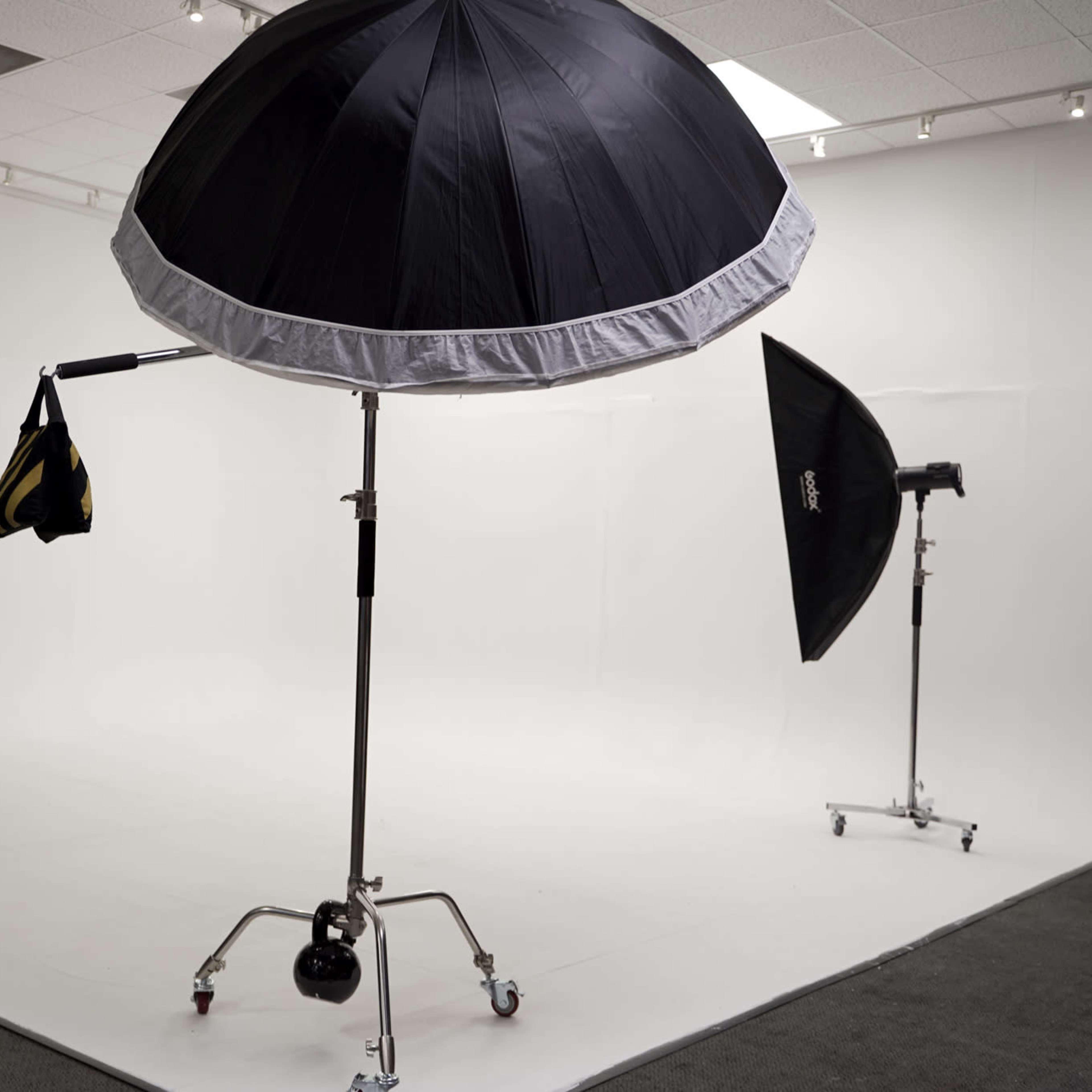 A photography studio with three light umbrellas set up on stands against a white backdrop.