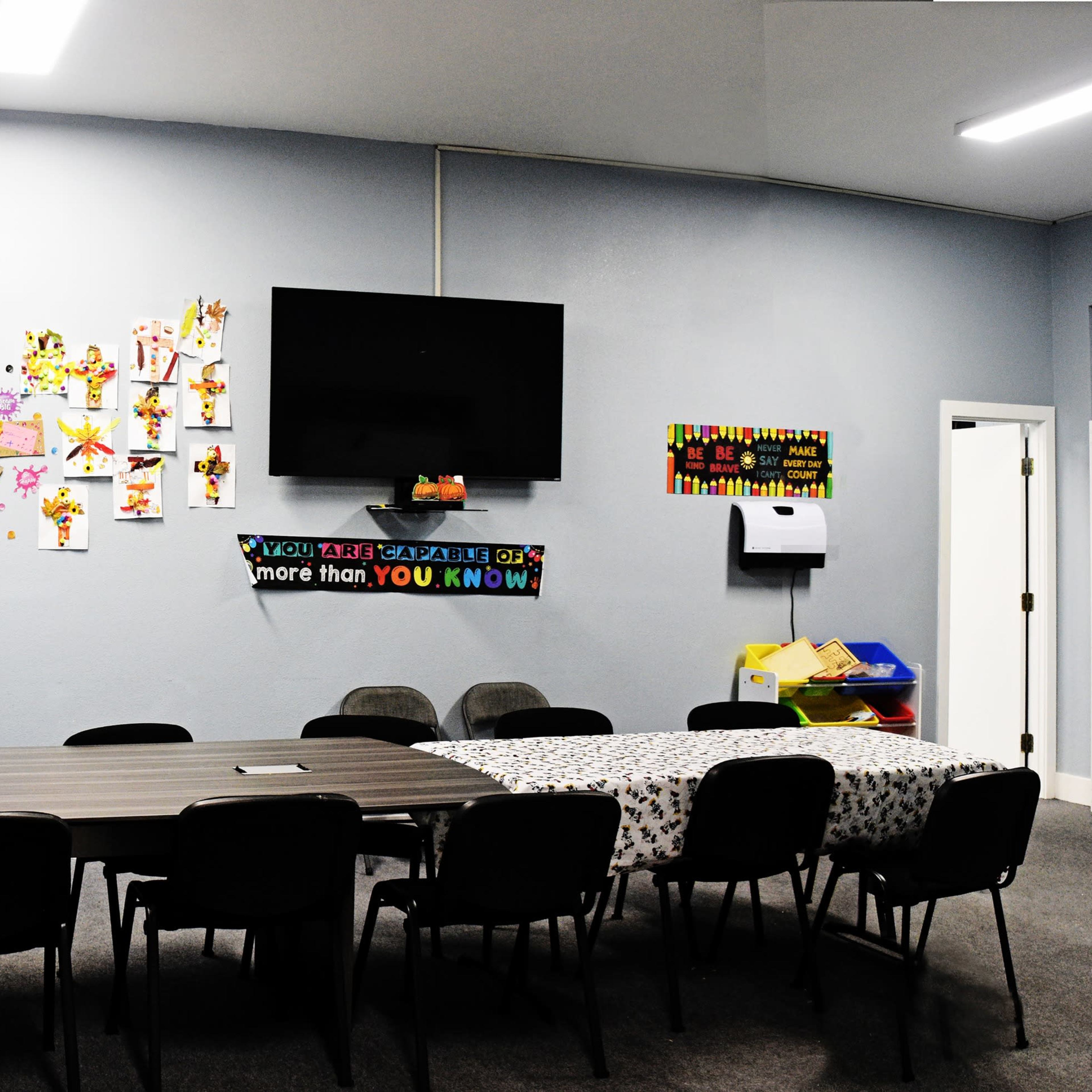 A rectangular table with chairs is positioned in a room adorned with colorful decorations, a wall-mounted TV, and various wall hangings.