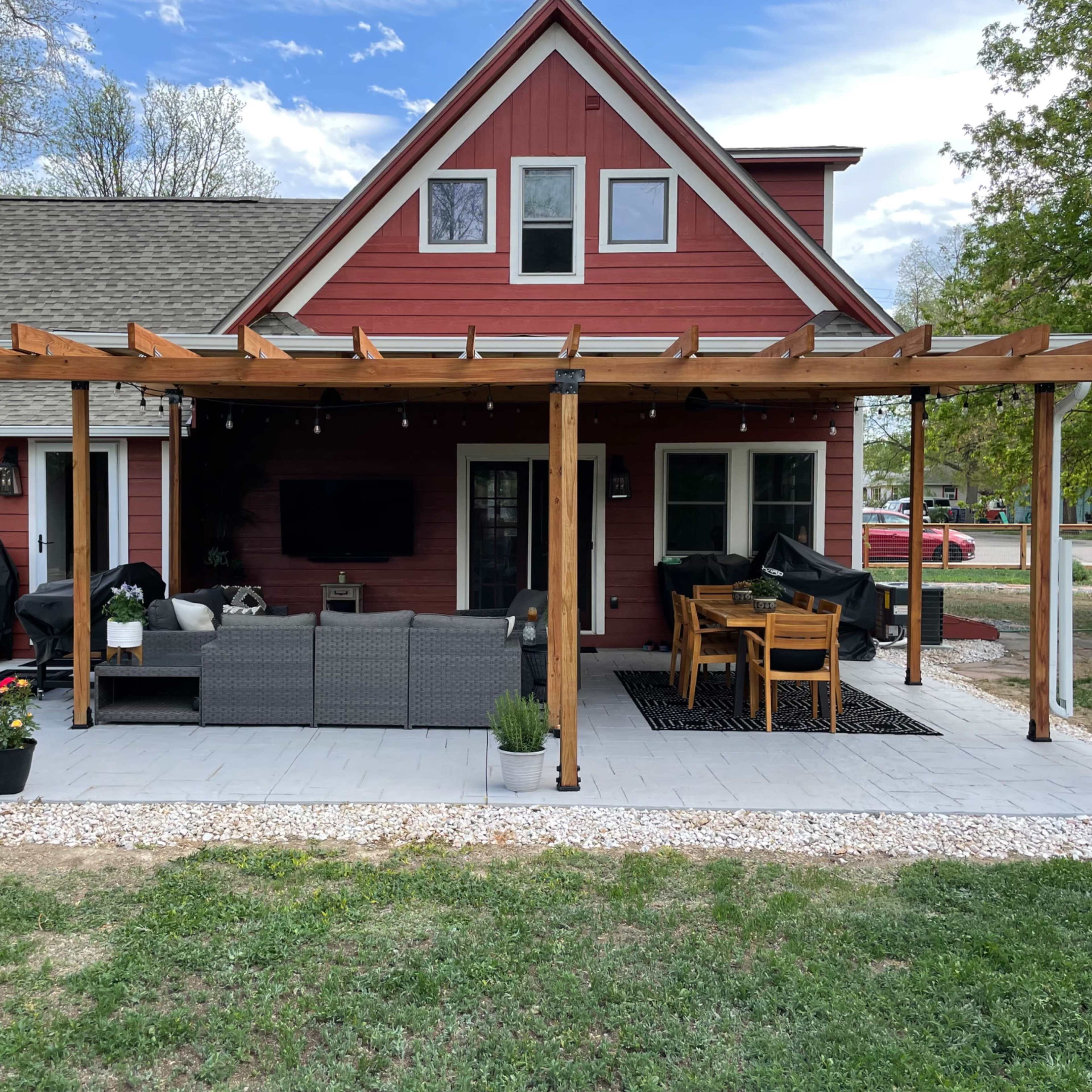 A red two-story house with a covered outdoor patio featuring a seating area and a dining table.