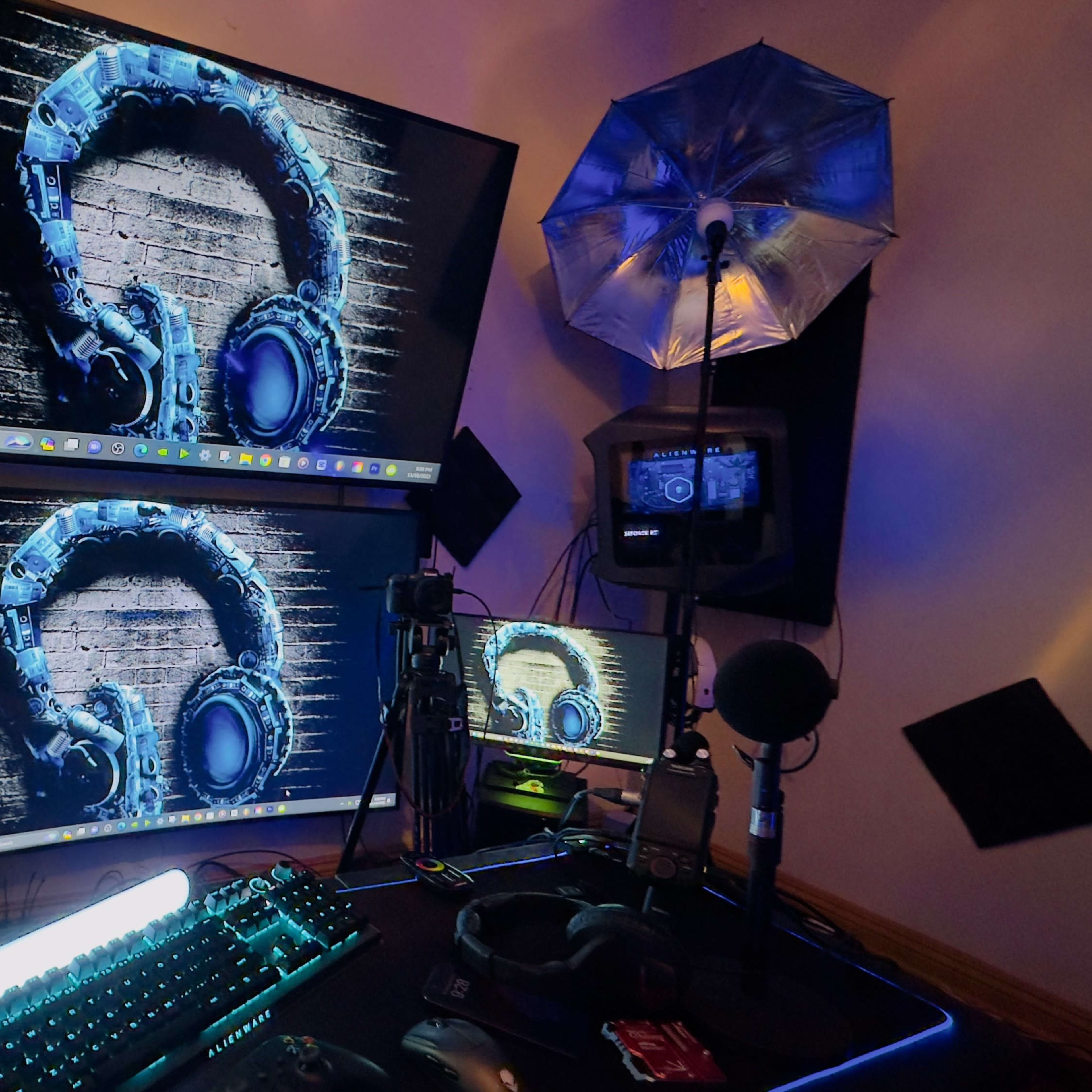 A multi-monitor computer setup featuring graphic designs of headphones on the screens, accompanied by a microphone and light umbrella.