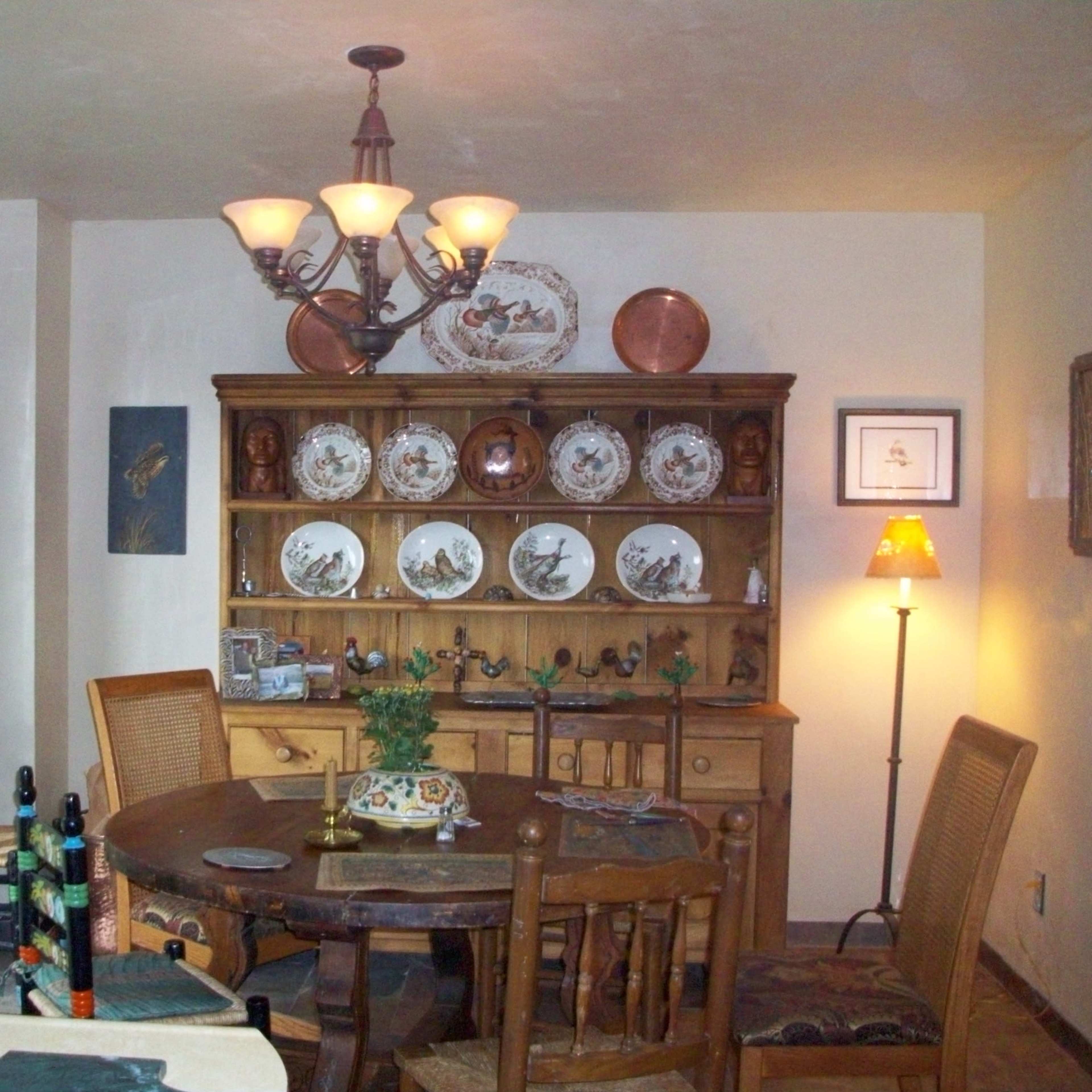 A dining area featuring a round wooden table, a china hutch displaying decorative plates, and a light fixture hanging from the ceiling.