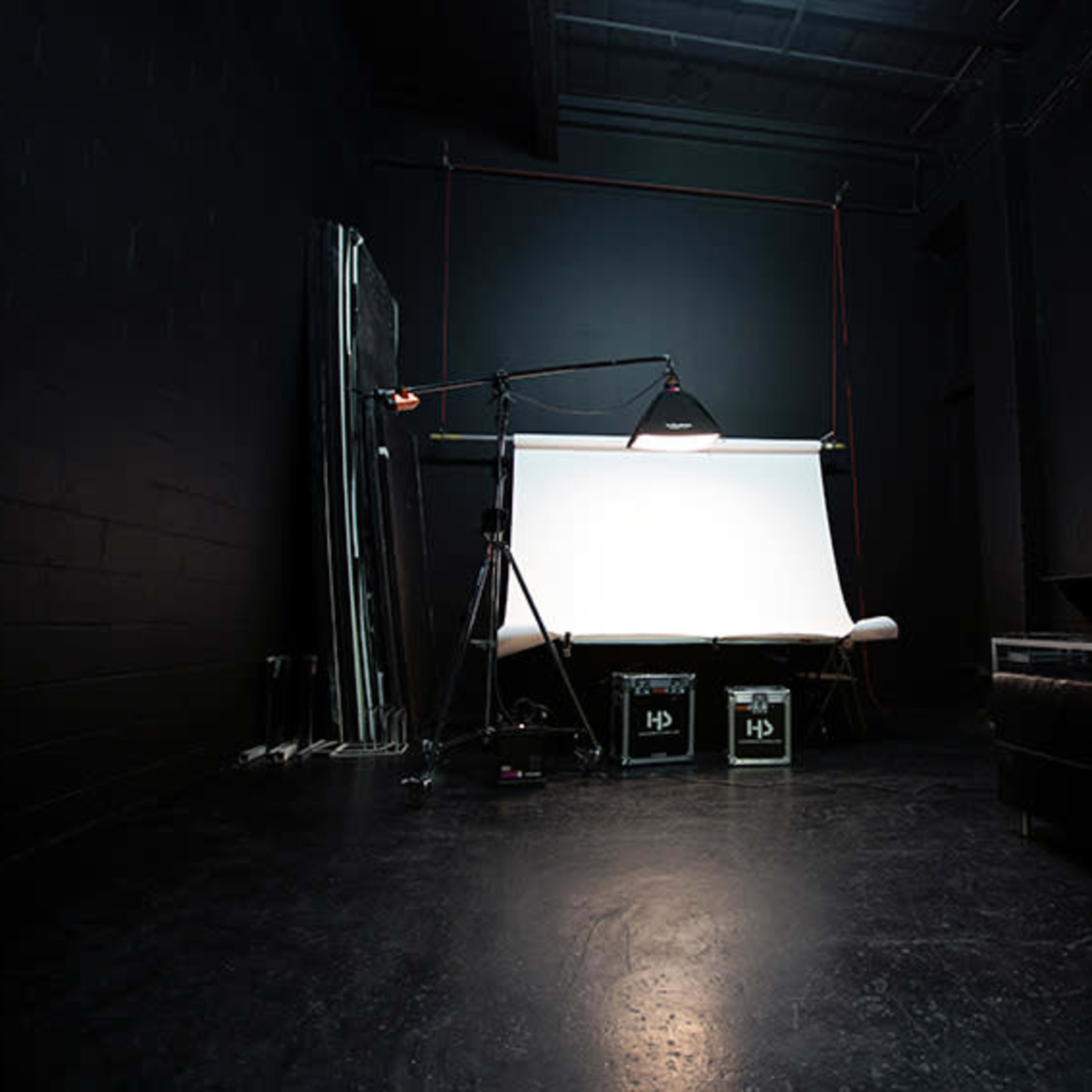 A dimly lit photography studio featuring a backdrop, lighting equipment, and storage boxes.
