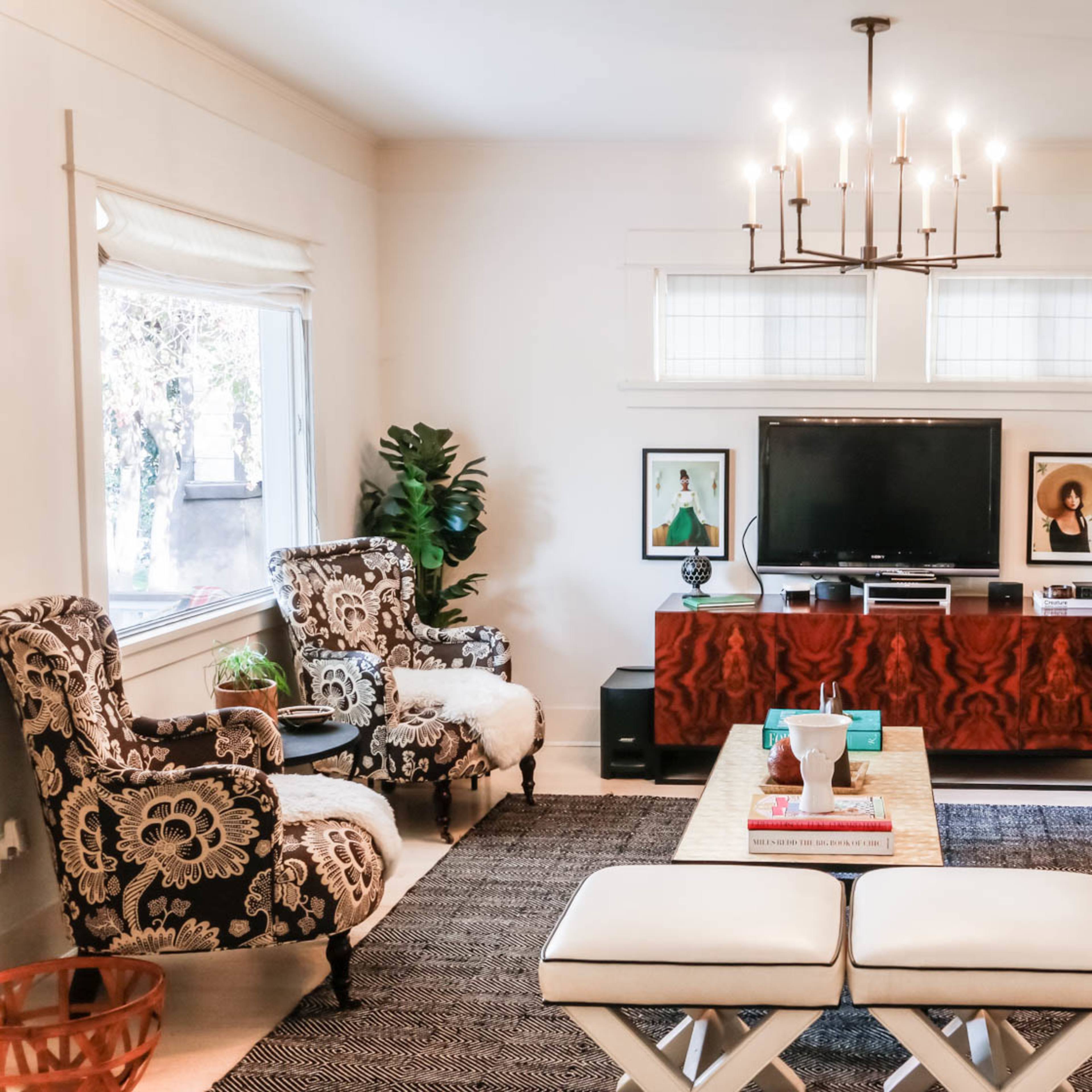 A living room features a green sofa, a wooden media console with a television, two patterned armchairs, and a coffee table on a textured rug.
