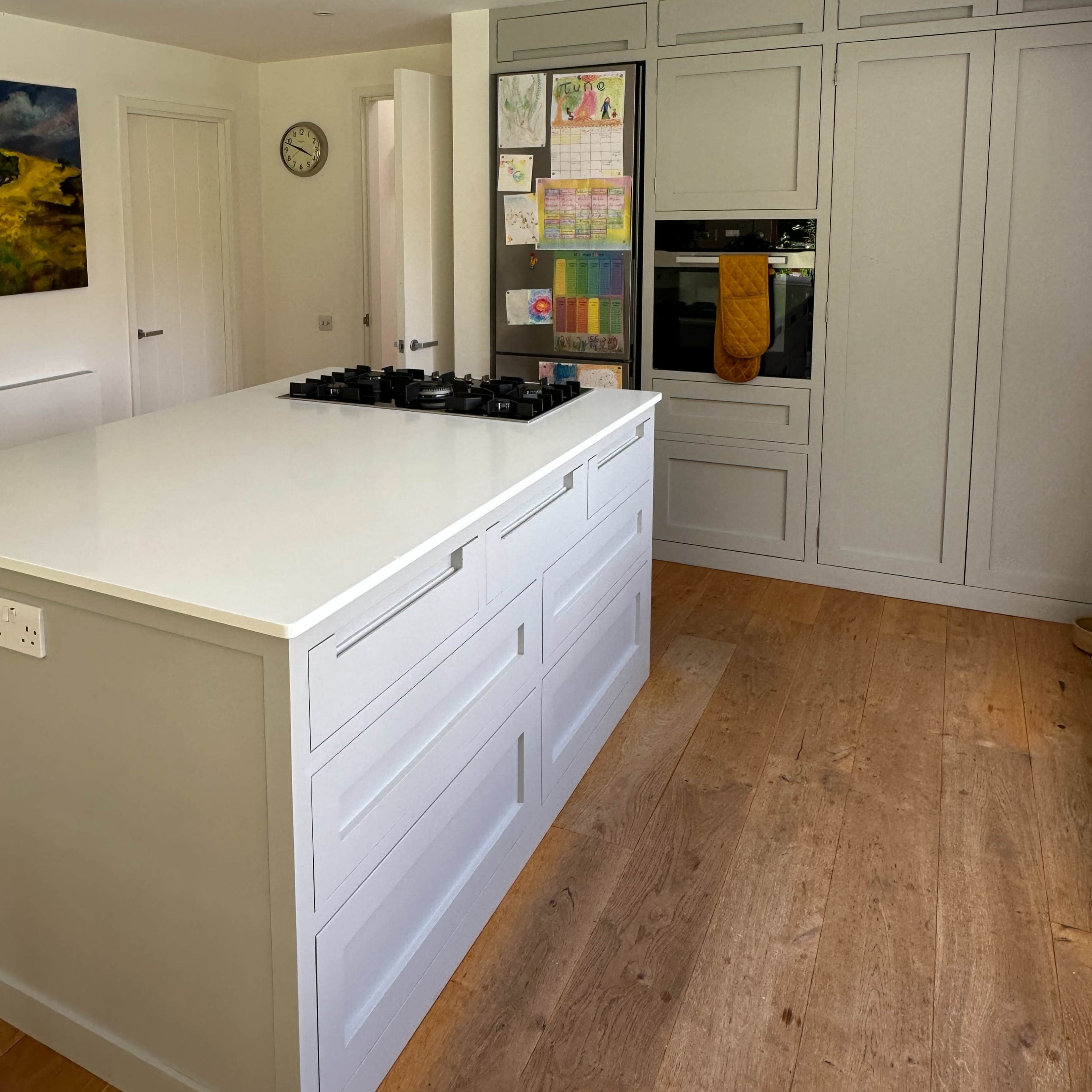 A modern kitchen features a central island with a gas cooktop, white cabinetry, and large windows allowing natural light.