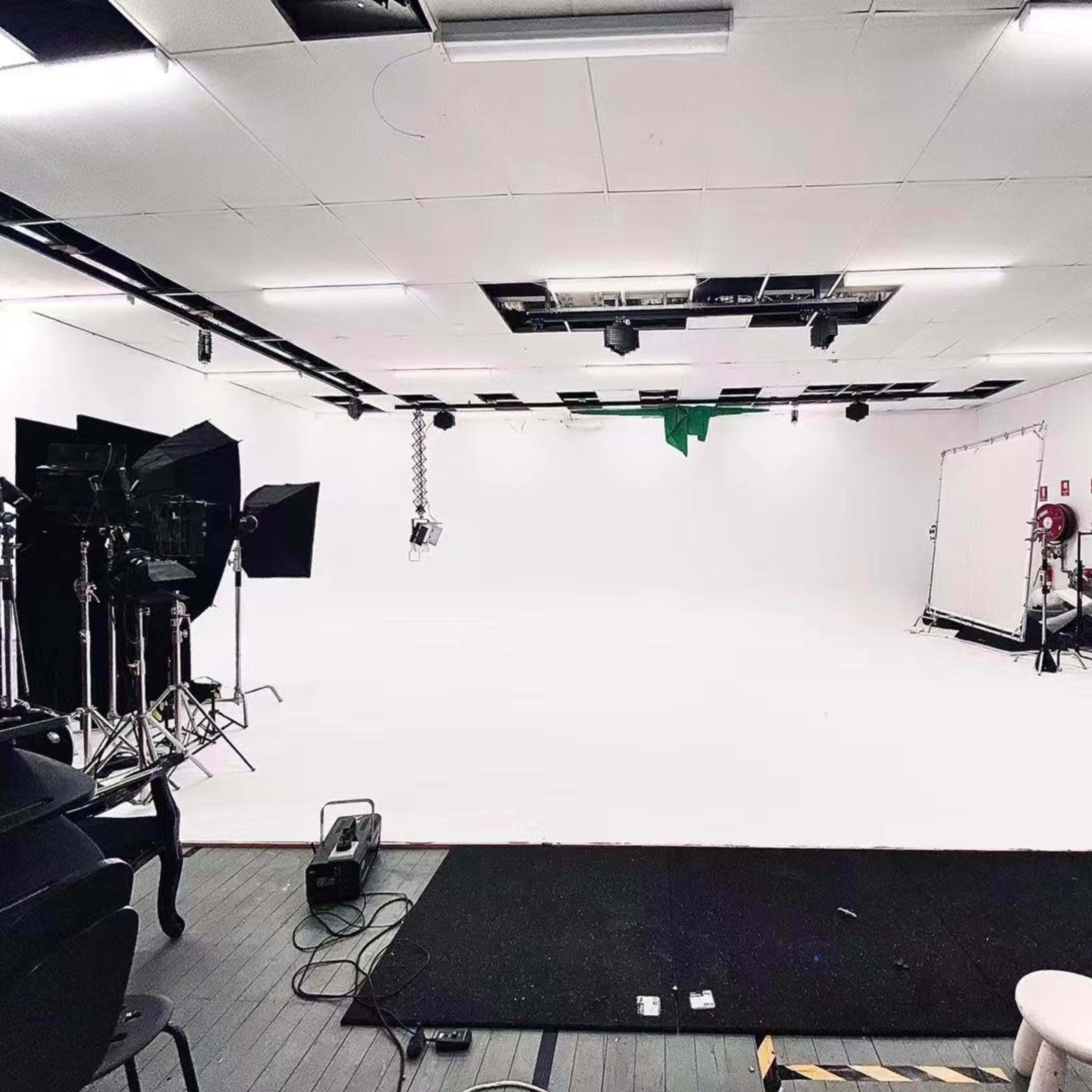 A spacious studio setup with white walls and floor, equipped with lighting equipment and a green screen in the background.