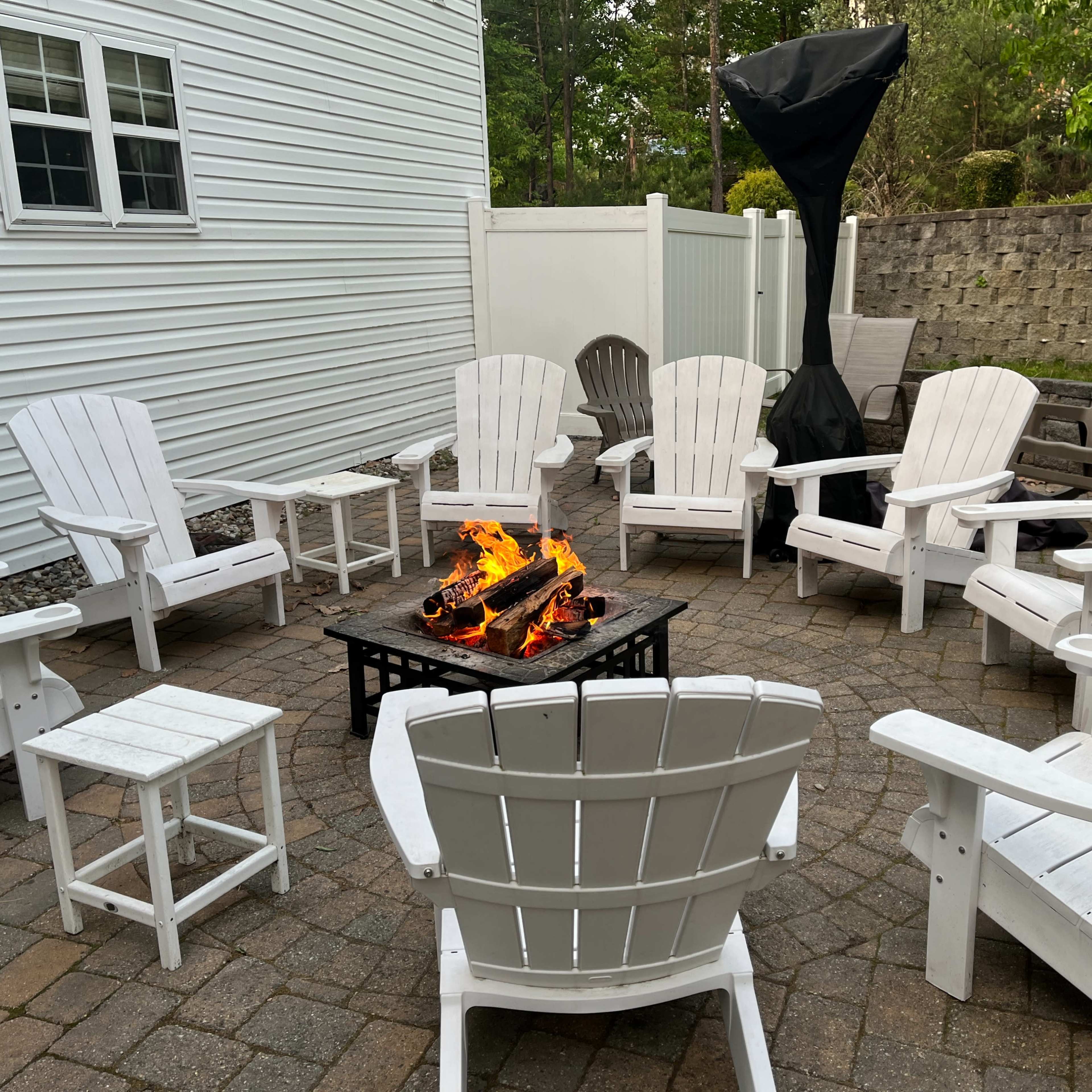 A circular seating area with white Adirondack chairs surrounds a fire pit, set on a stone patio.