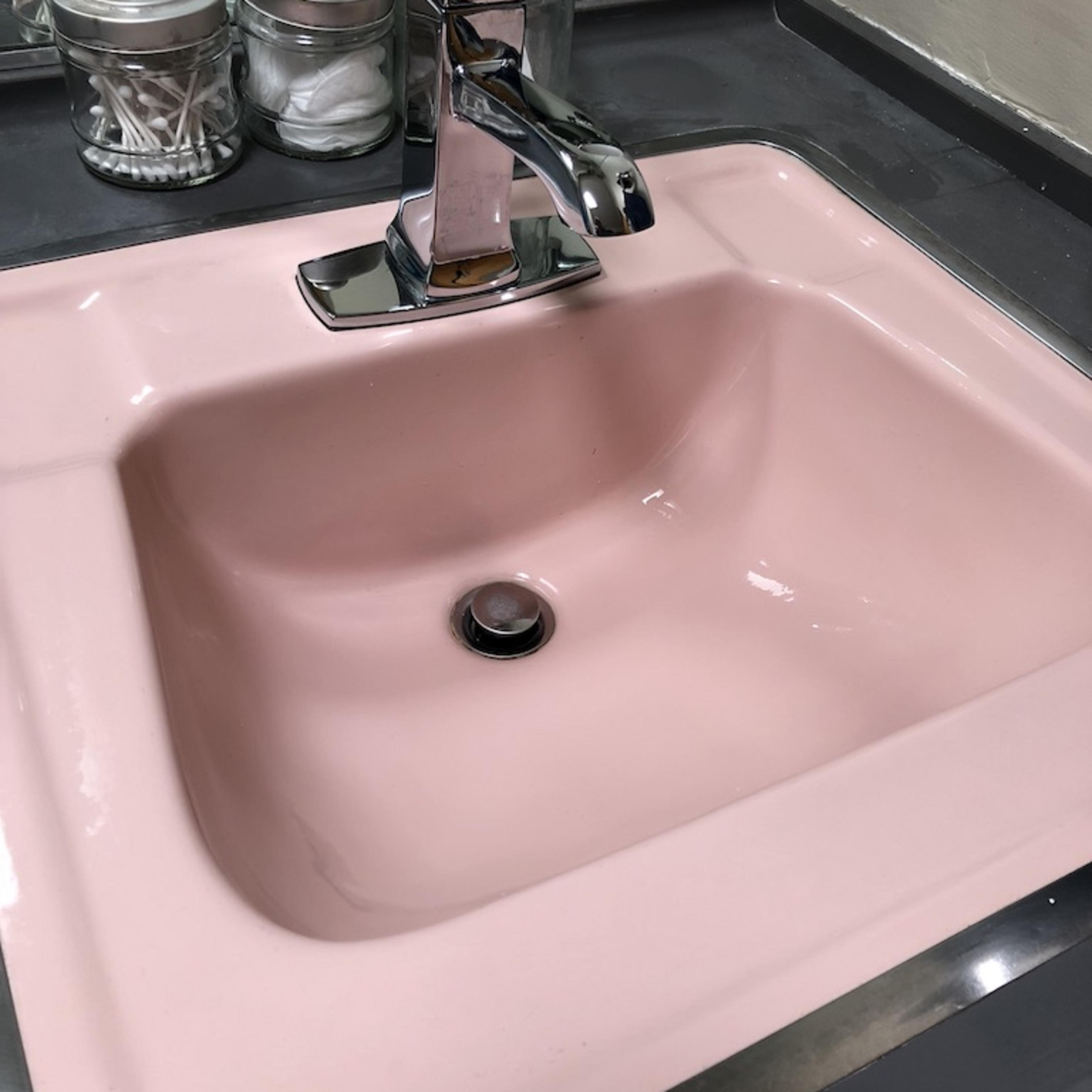 A pink sink, with a shiny faucet and glass containers holding toiletries, set against a dark countertop.