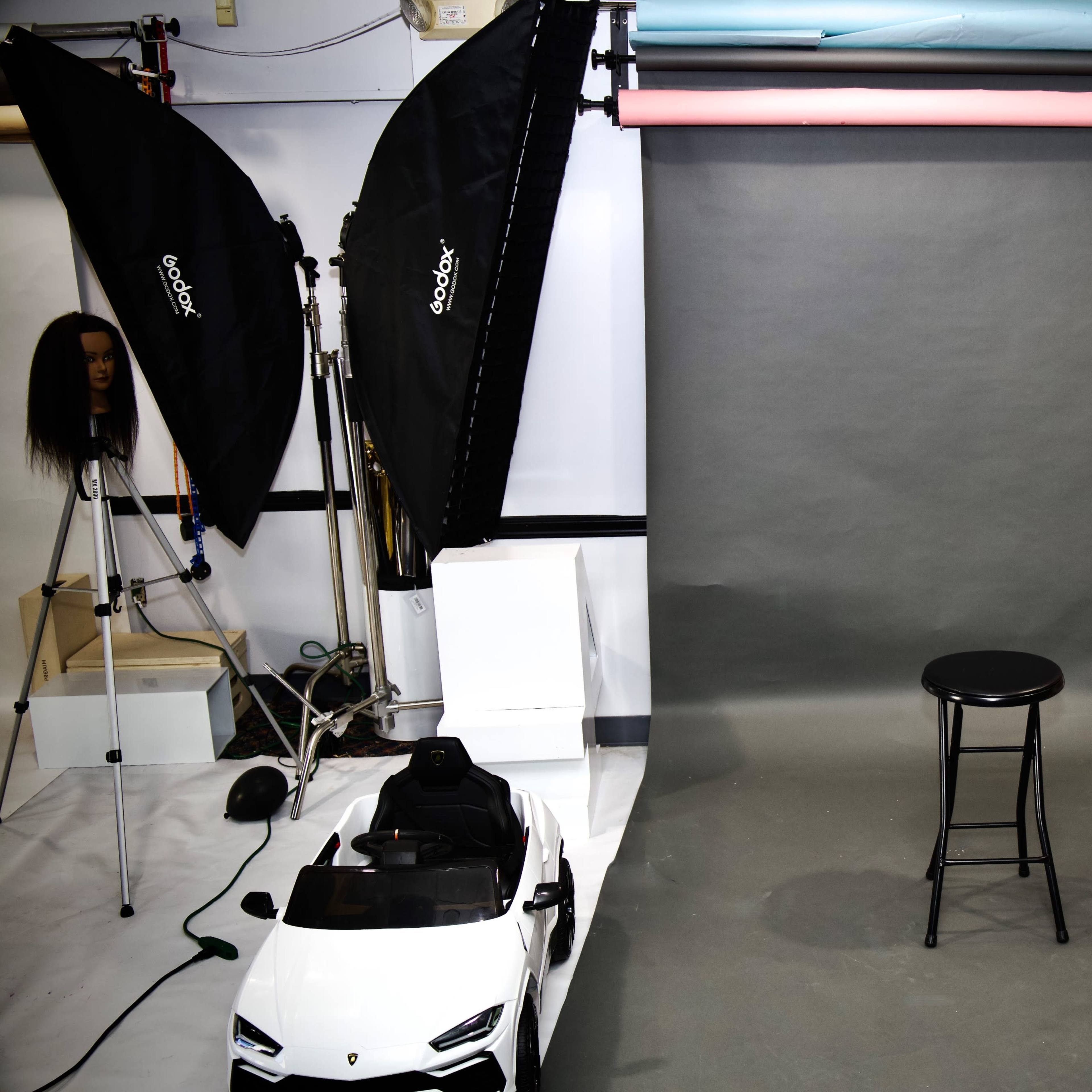 A photography studio setup with a gray backdrop, a black stool, and multiple softbox lights, along with a toy car positioned nearby.