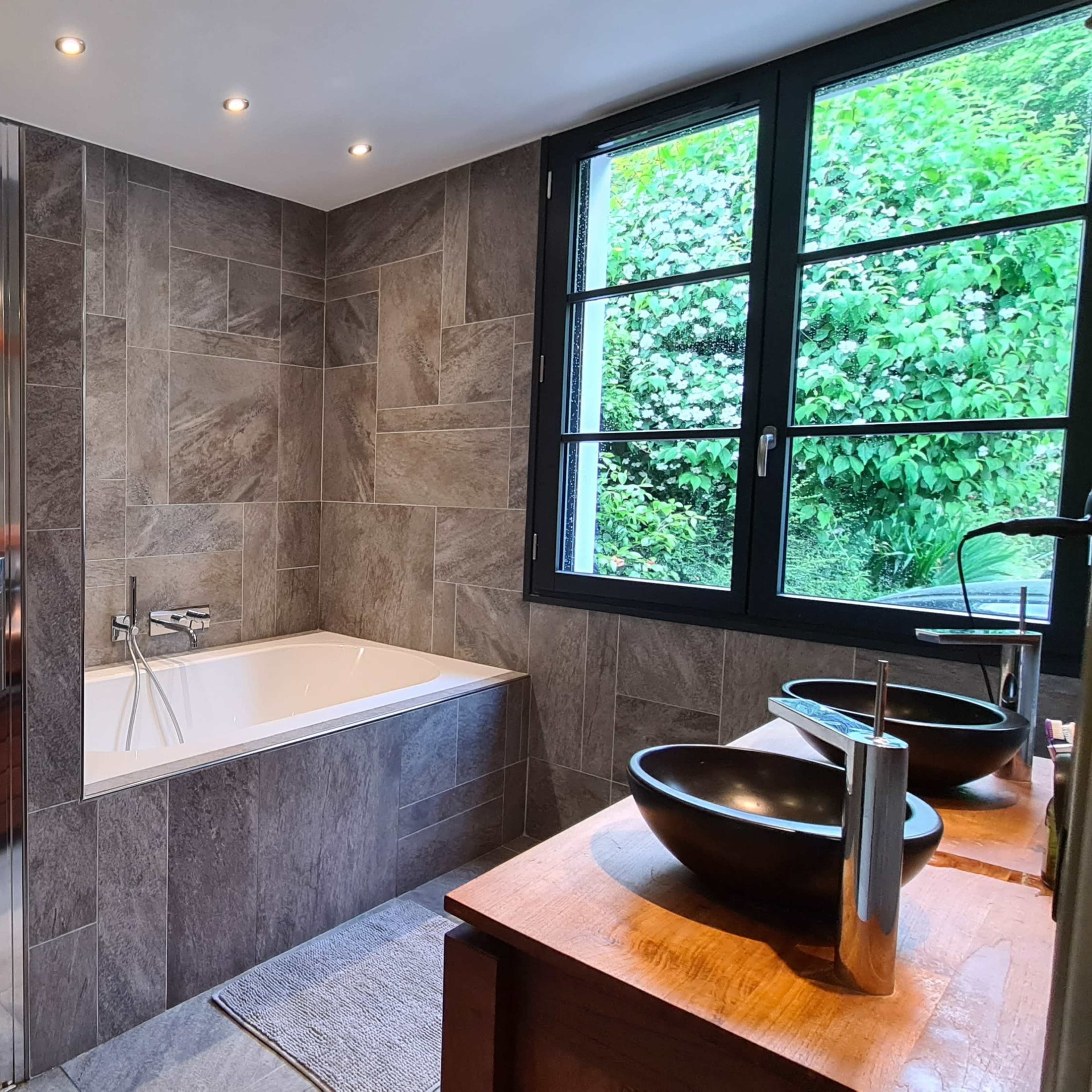 A modern bathroom featuring a glass shower enclosure, a freestanding bathtub, and double pedestal sinks with a wooden counter.