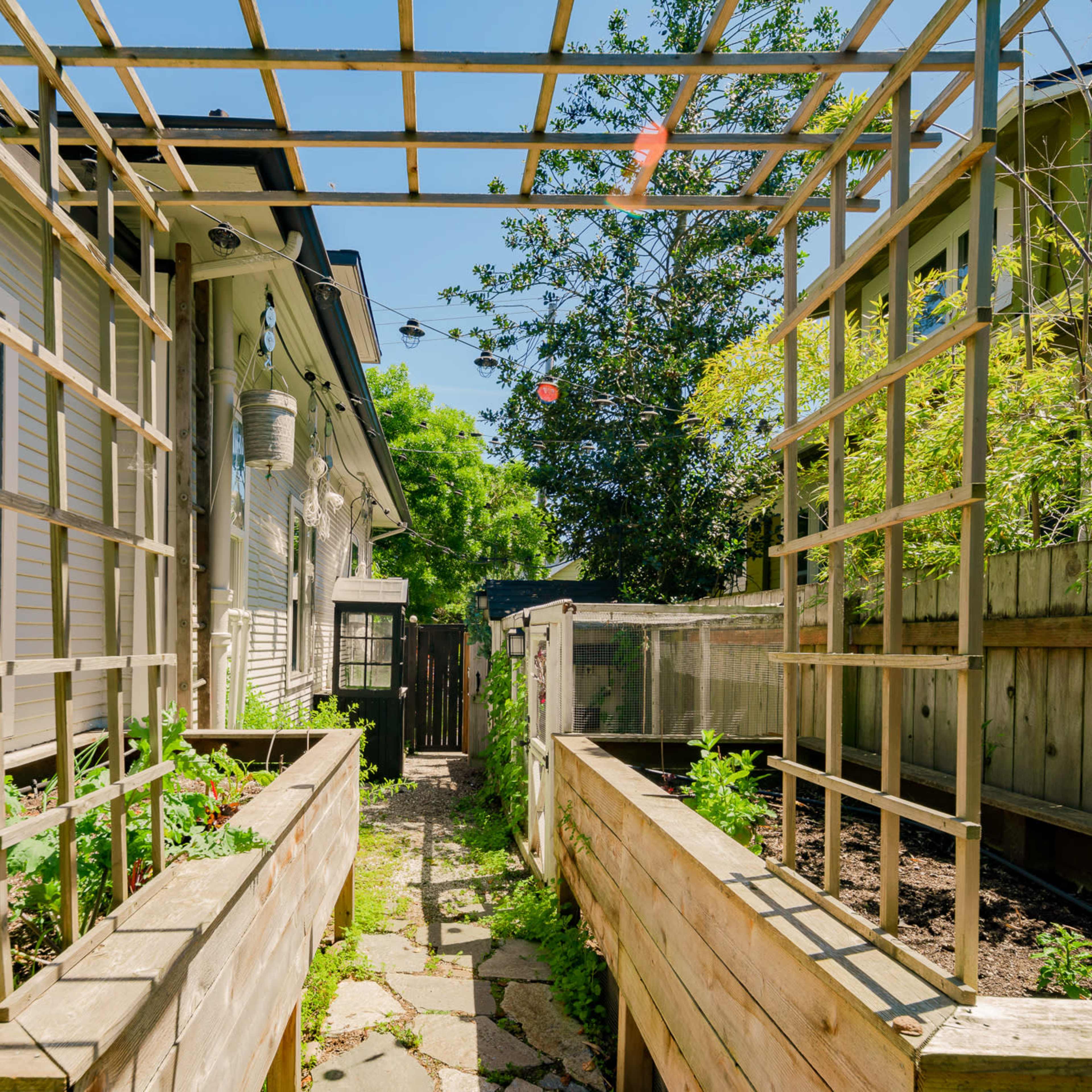 A narrow garden pathway lined with raised wooden planting beds on either side, leading to a fence with greenery in the background.
