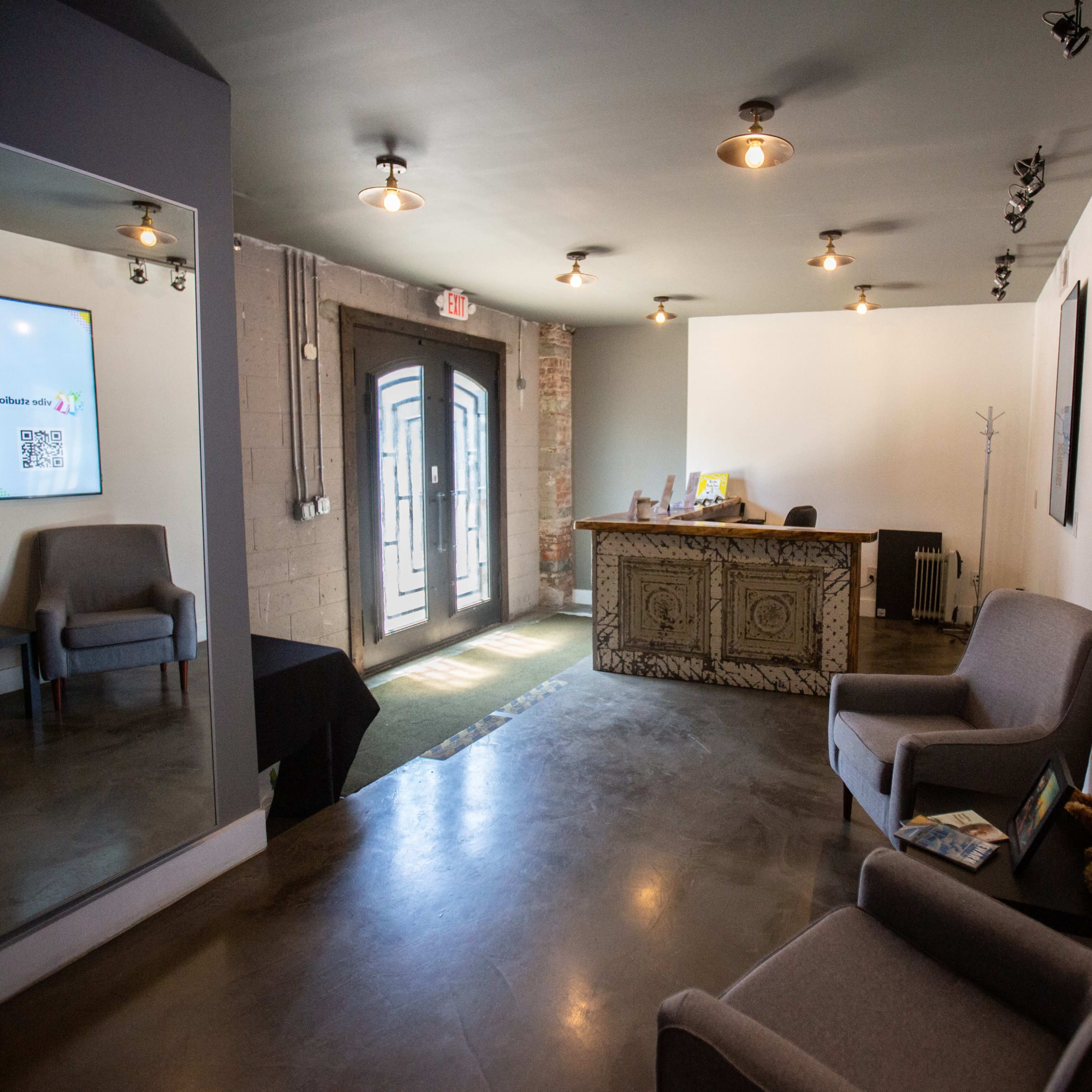 A modern reception area with two gray chairs, a decorative front desk, and digital displays on the walls.
