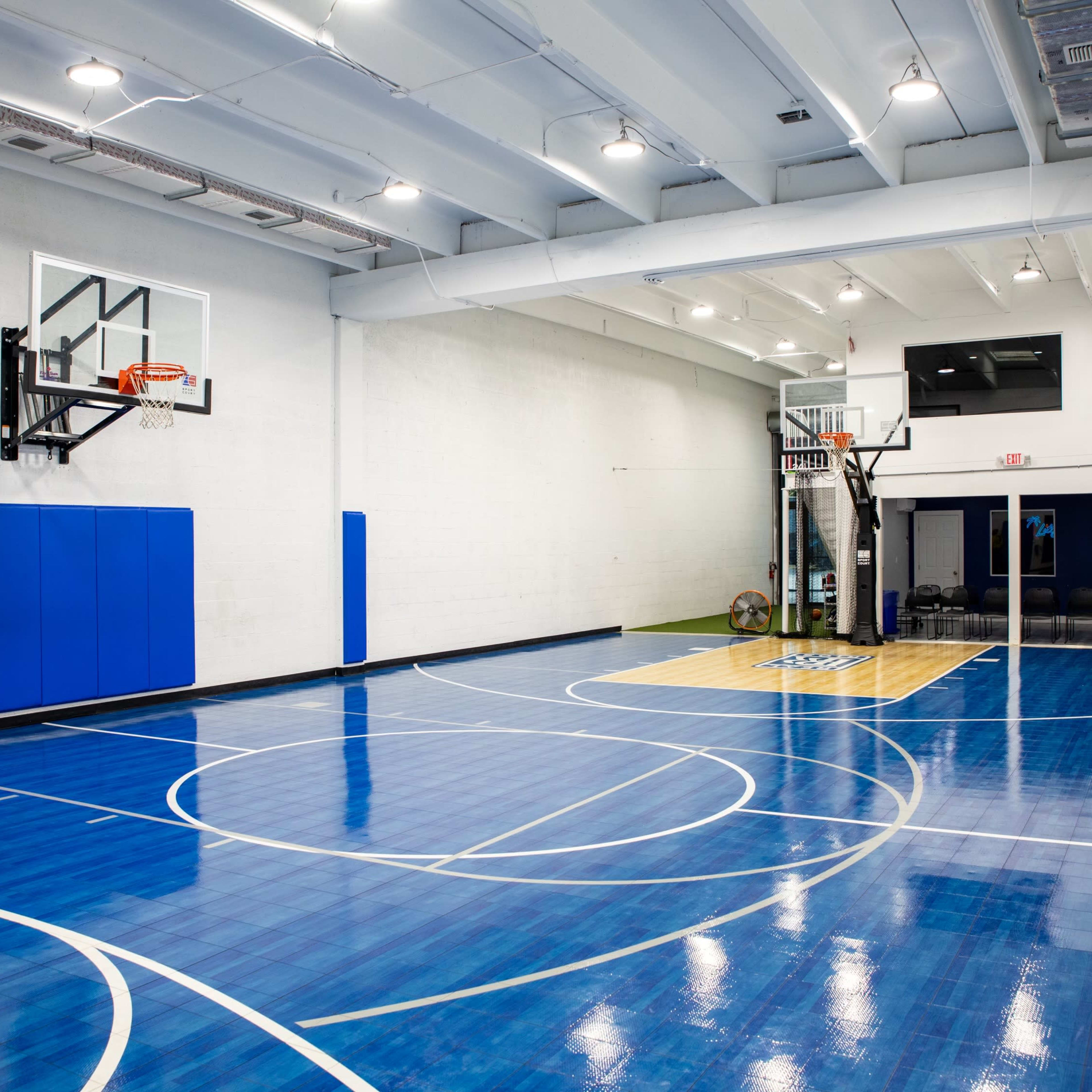 A basketball court with a blue and yellow floor, a hoop mounted on the wall, and padded wall sections.