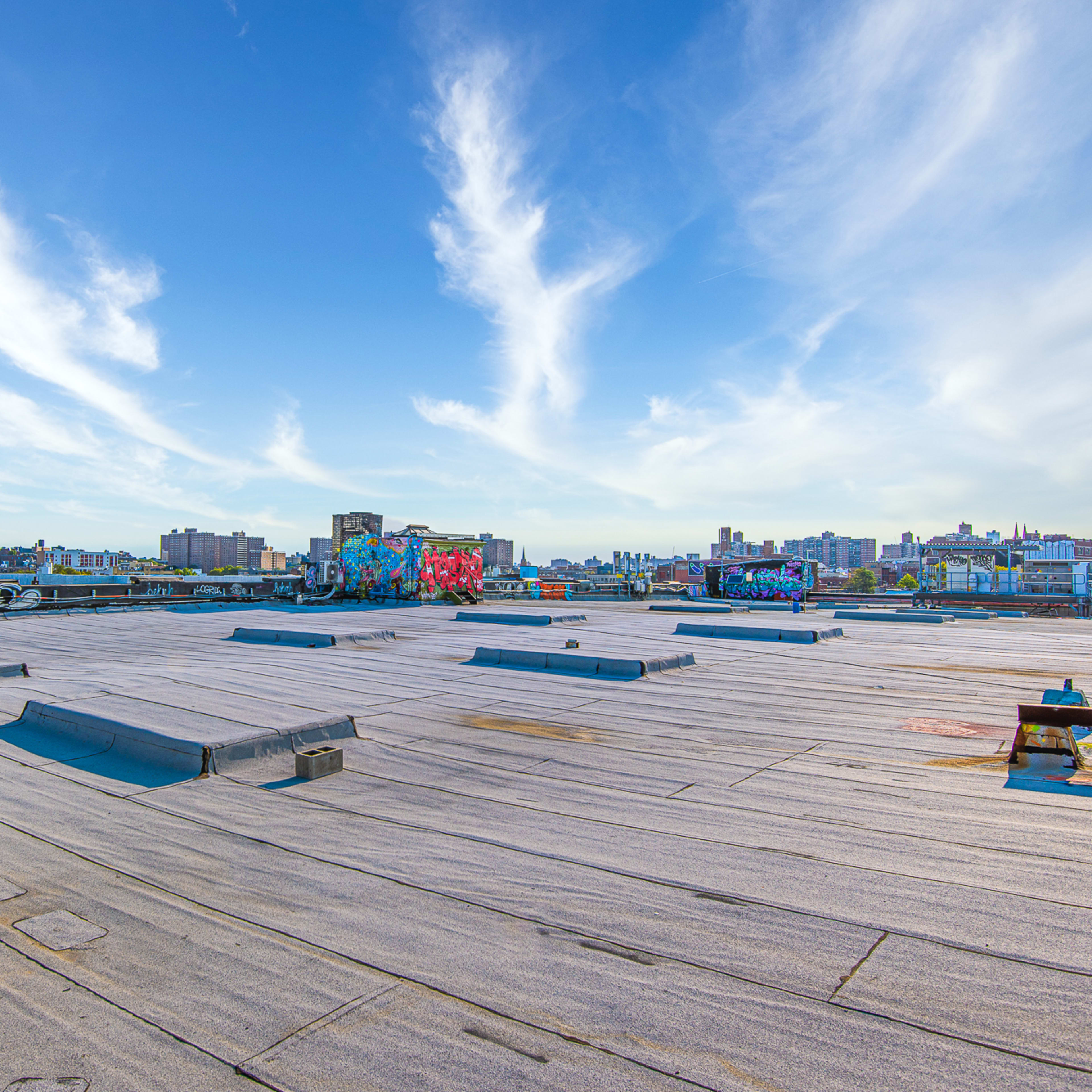 A rooftop scene with a flat surface, featuring graffiti art and a clear blue sky with wispy clouds in the background.