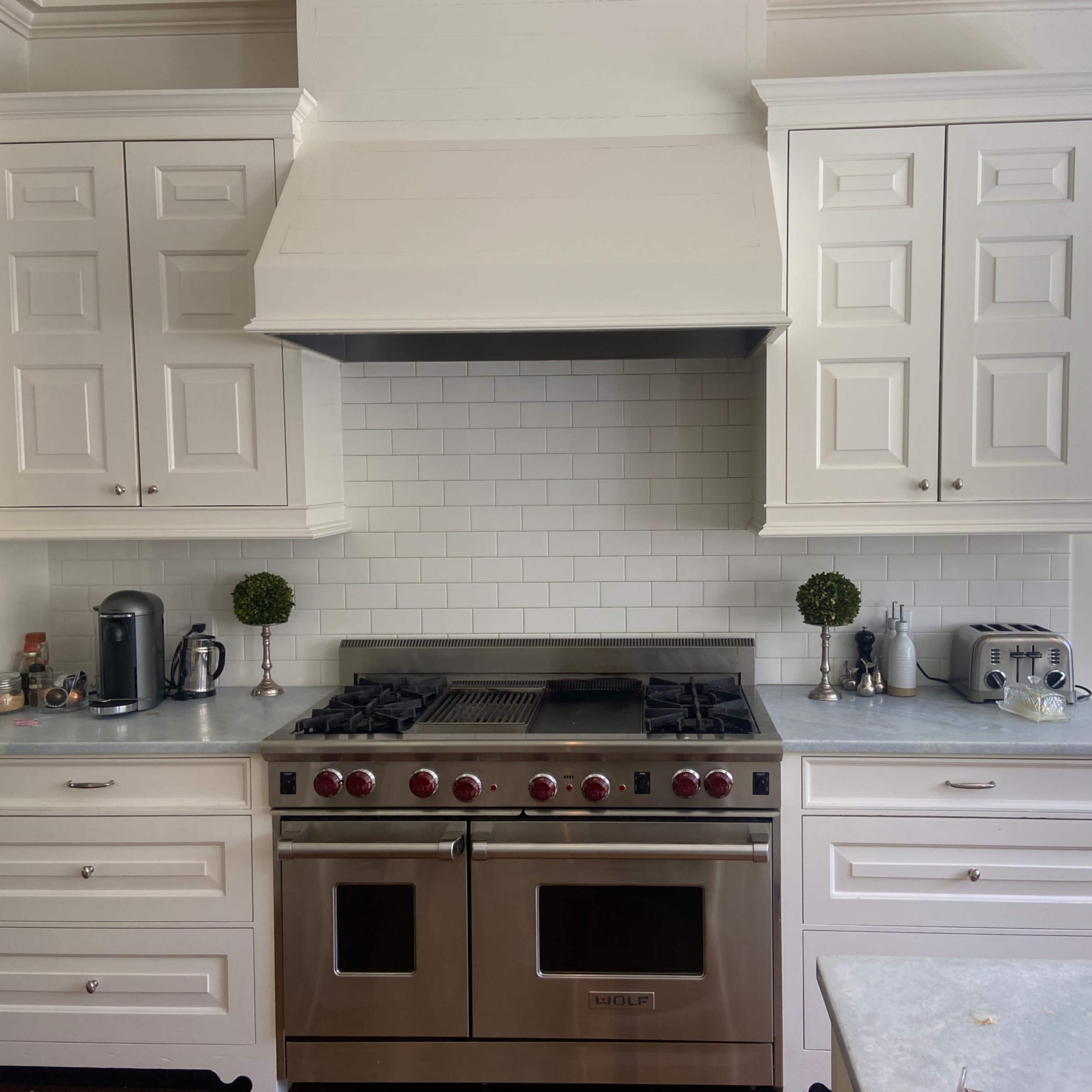 A modern kitchen features white cabinets, a stainless steel range hood, and a professional-grade gas stove surrounded by light-colored countertops.