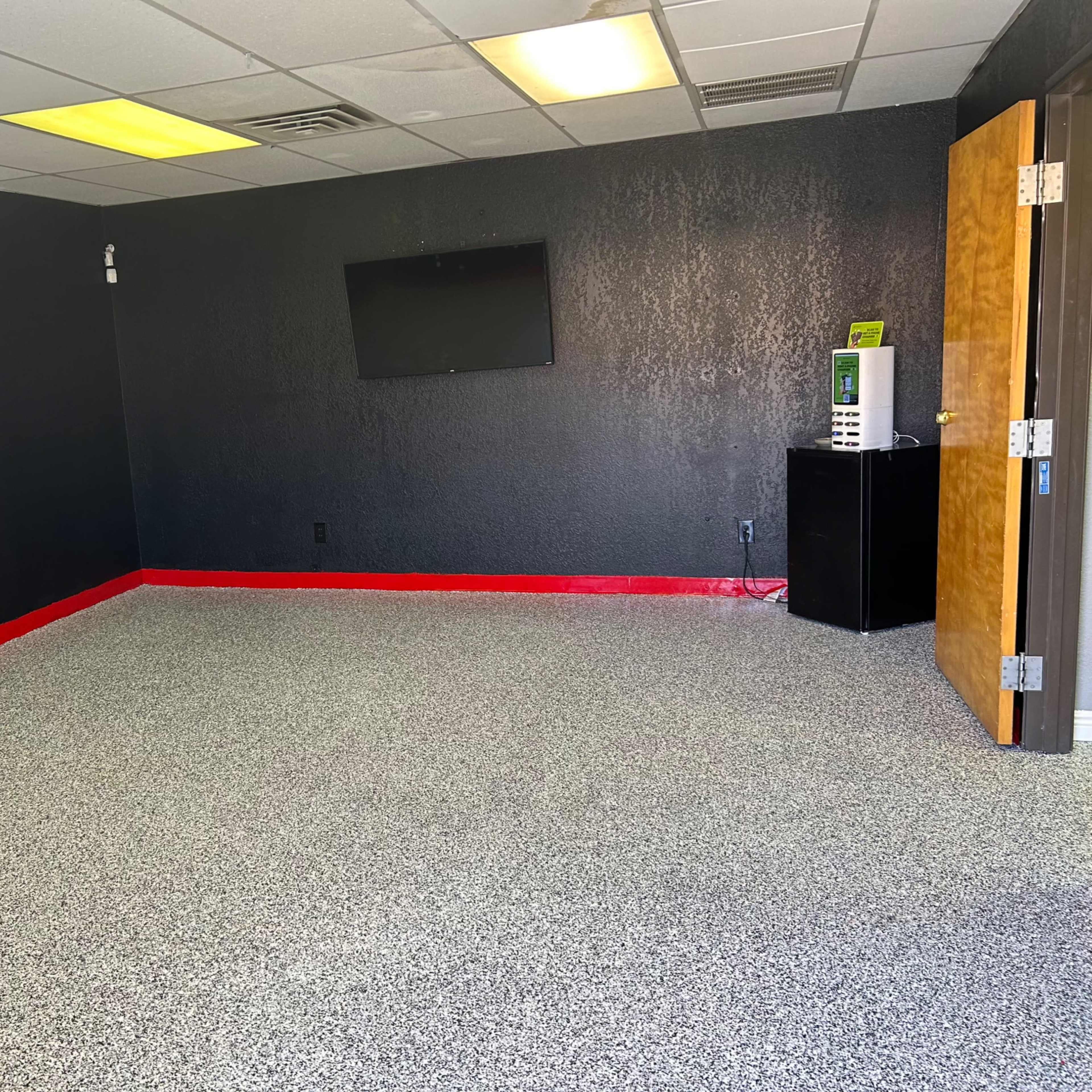 A sparse room with black walls, a red baseboard, a small wall-mounted TV, a microwave, and an open door.
