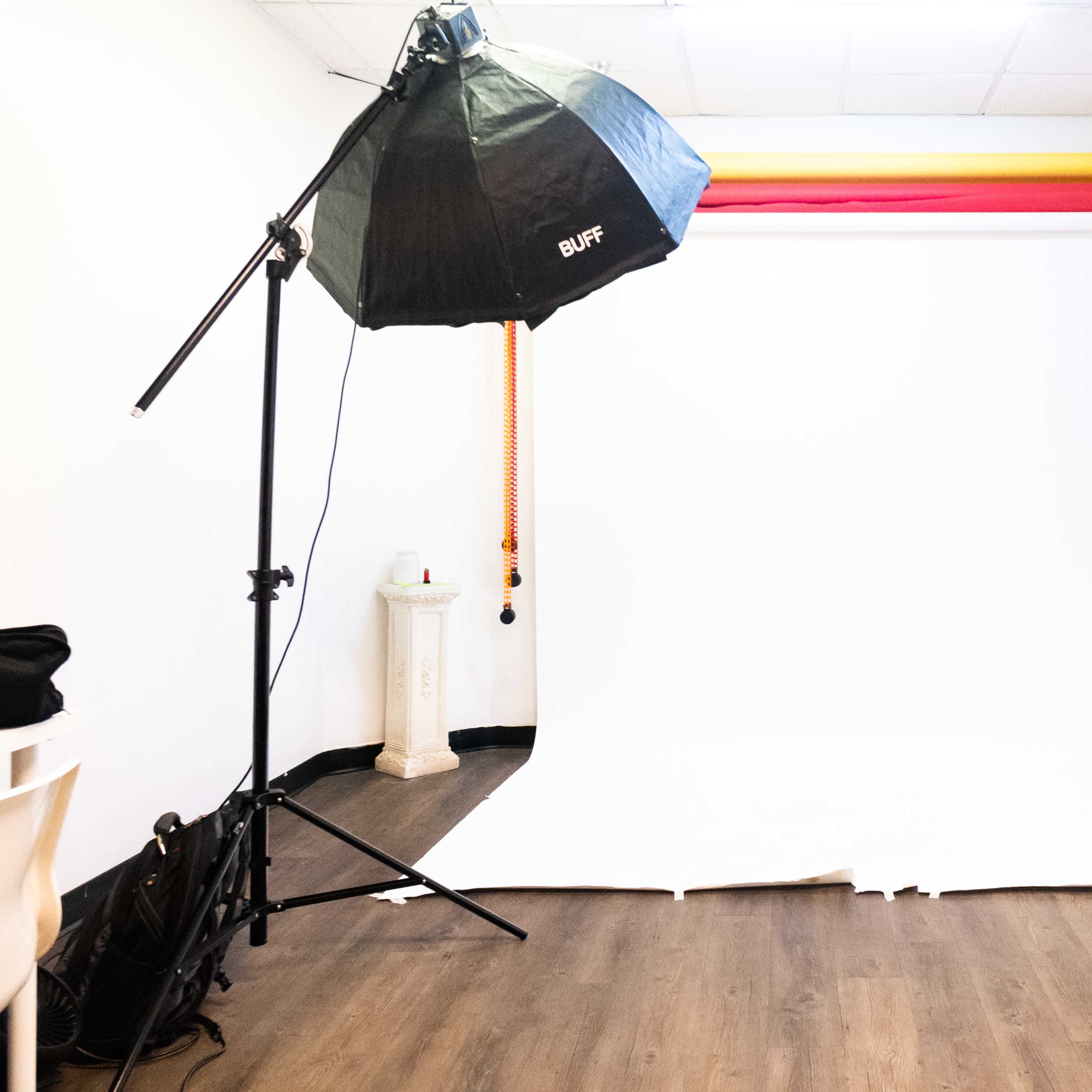 A photography studio with a white backdrop, a softbox light, and a wall adorned with a large cityscape print.