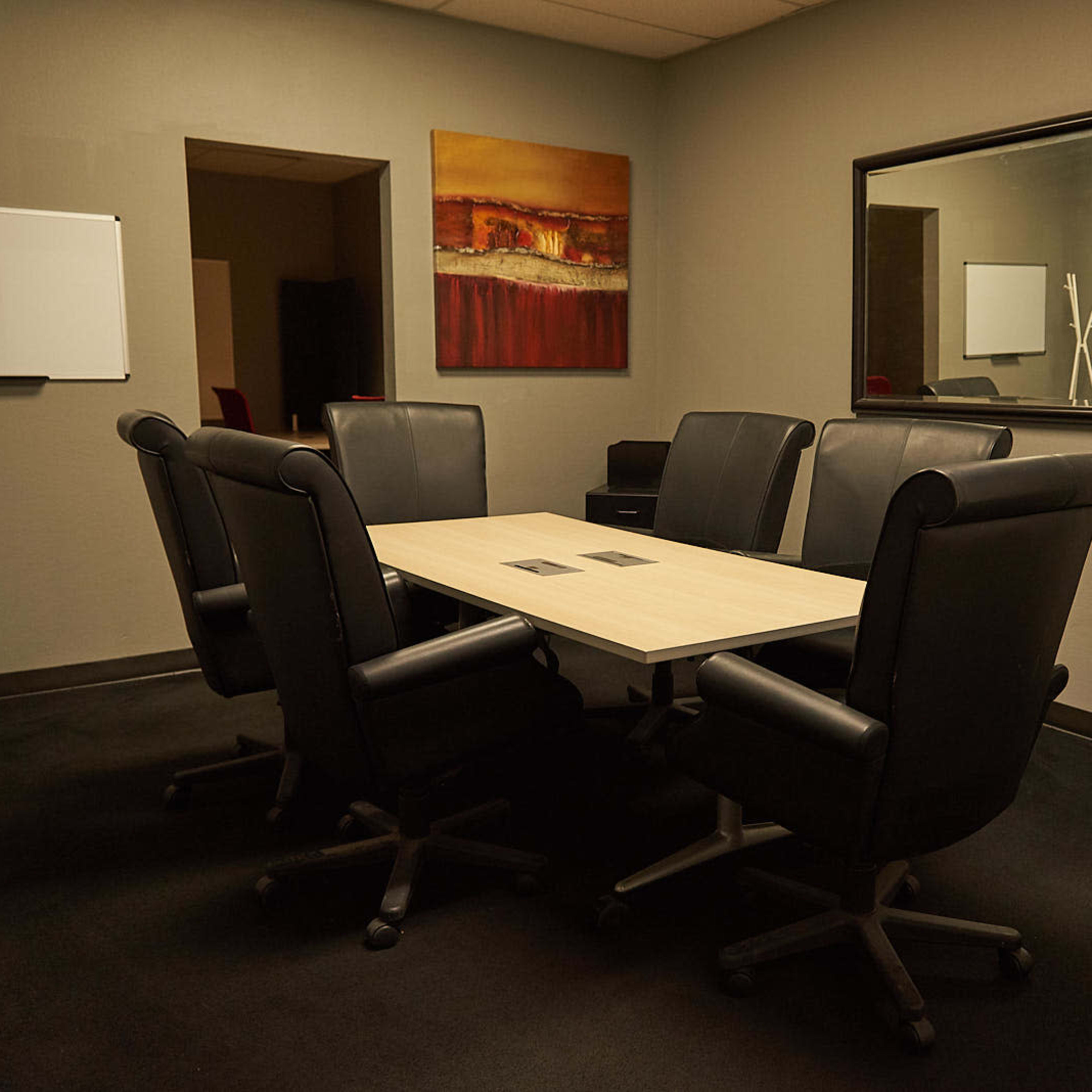 A conference room with a rectangular table surrounded by six black leather chairs, and a mirror reflecting the room's decor.
