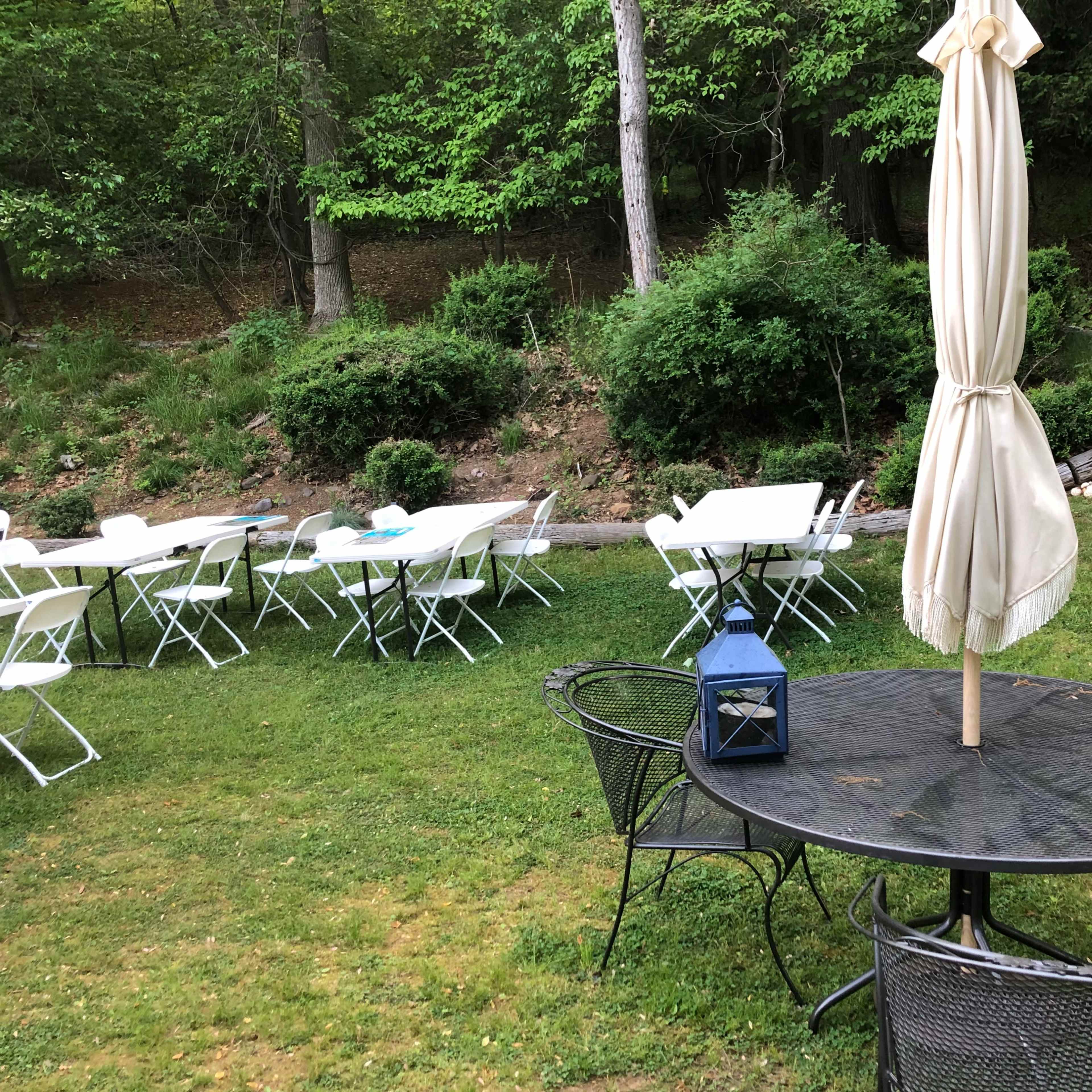 The scene shows a grassy outdoor area with several white tables and chairs arranged on the left, while a black round table and a blue lantern are positioned in the foreground.