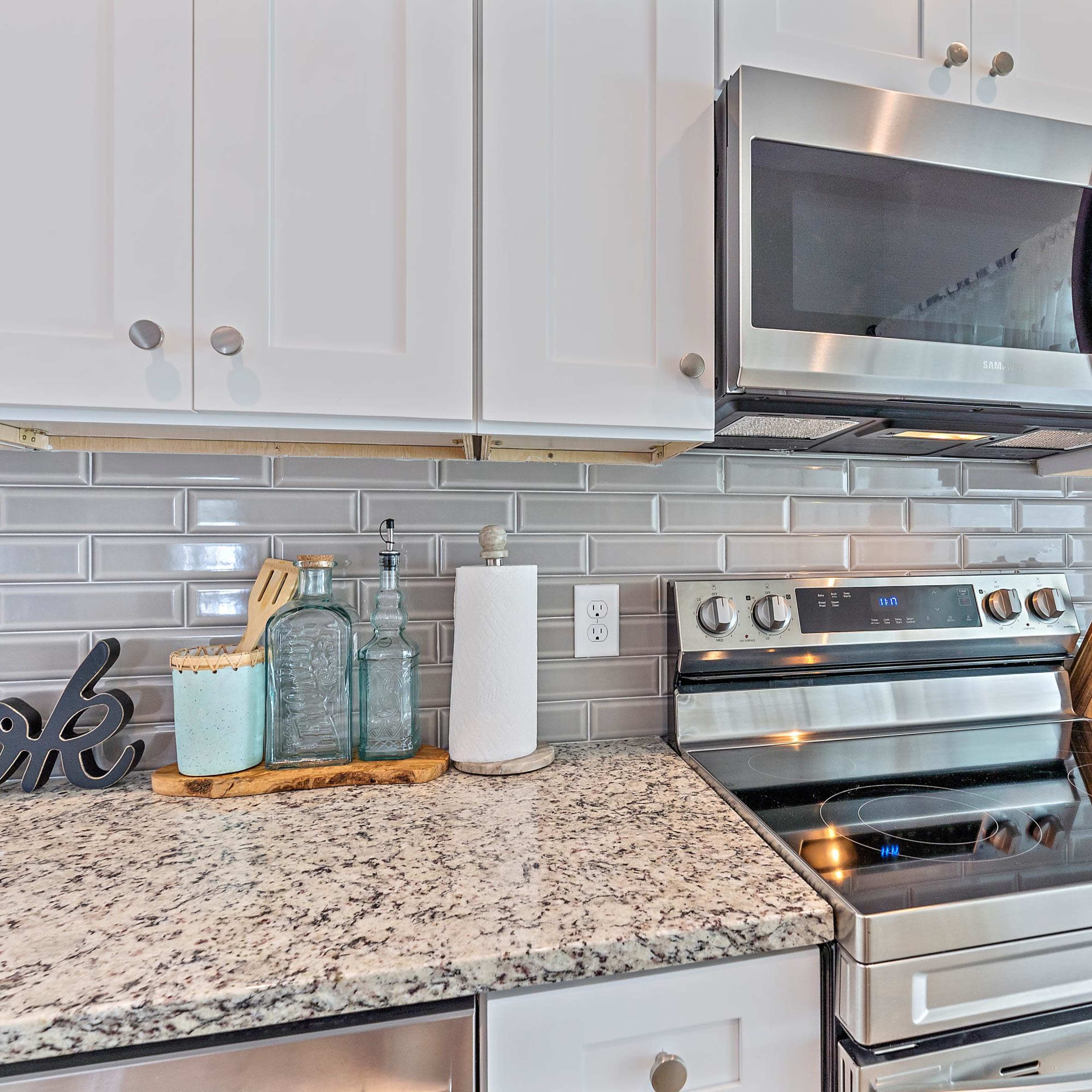 A modern kitchen countertop featuring a stainless steel stove, microwave, and various cooking utensils arranged on a granite surface.