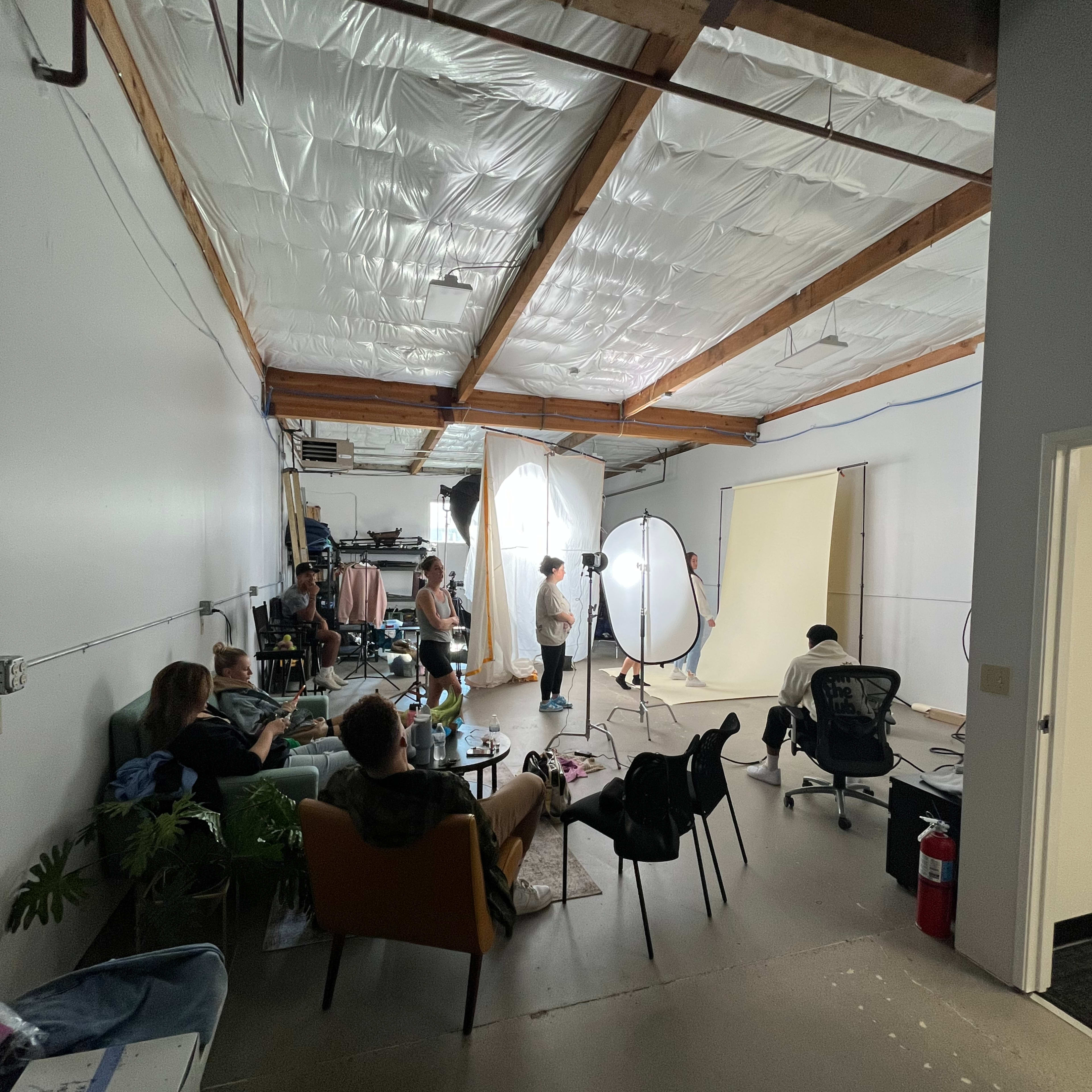A group of people is gathered in a spacious studio, with photography equipment set up and backdrops arranged for a photoshoot.
