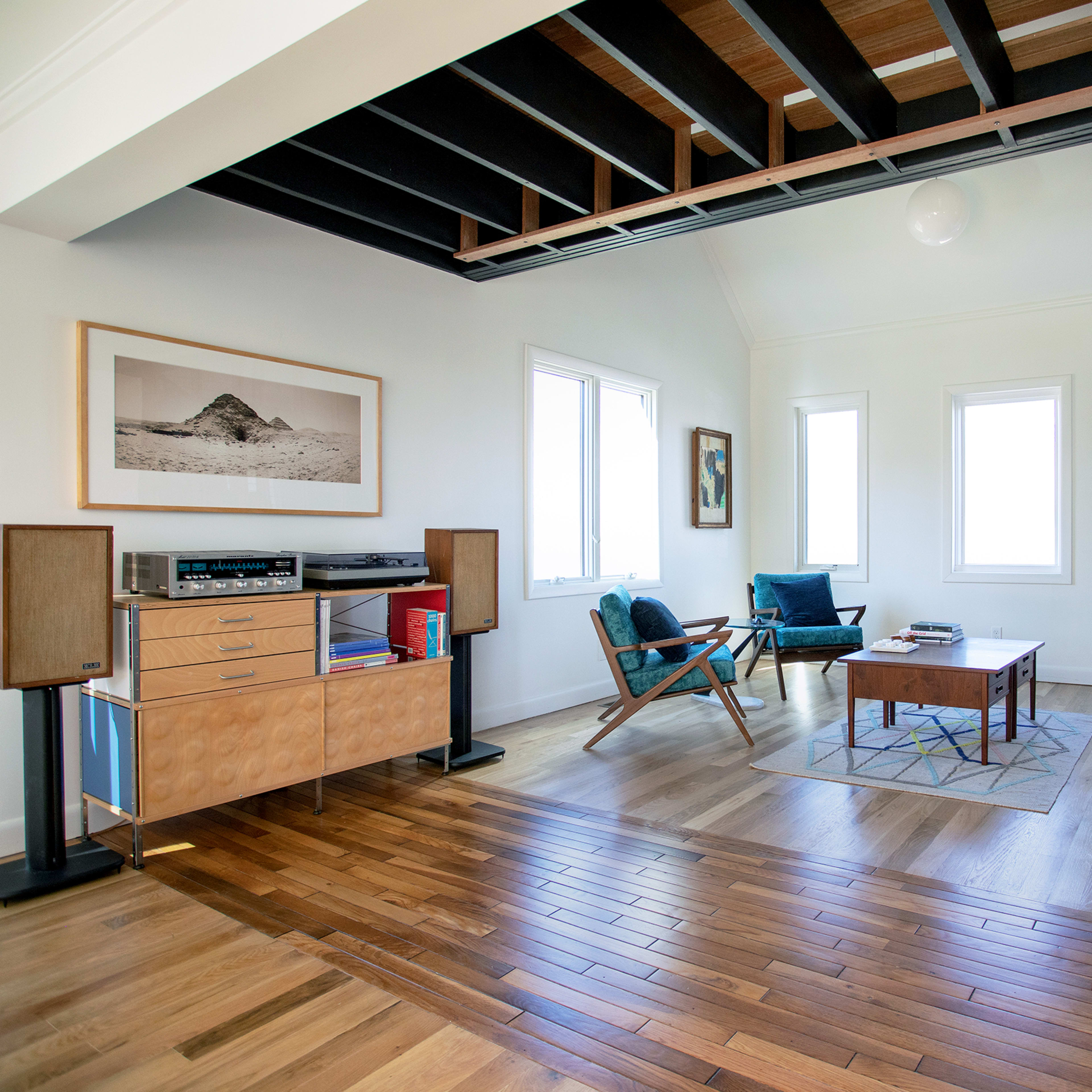 A modern living room with wooden floors, a coffee table, blue chairs, and large windows.