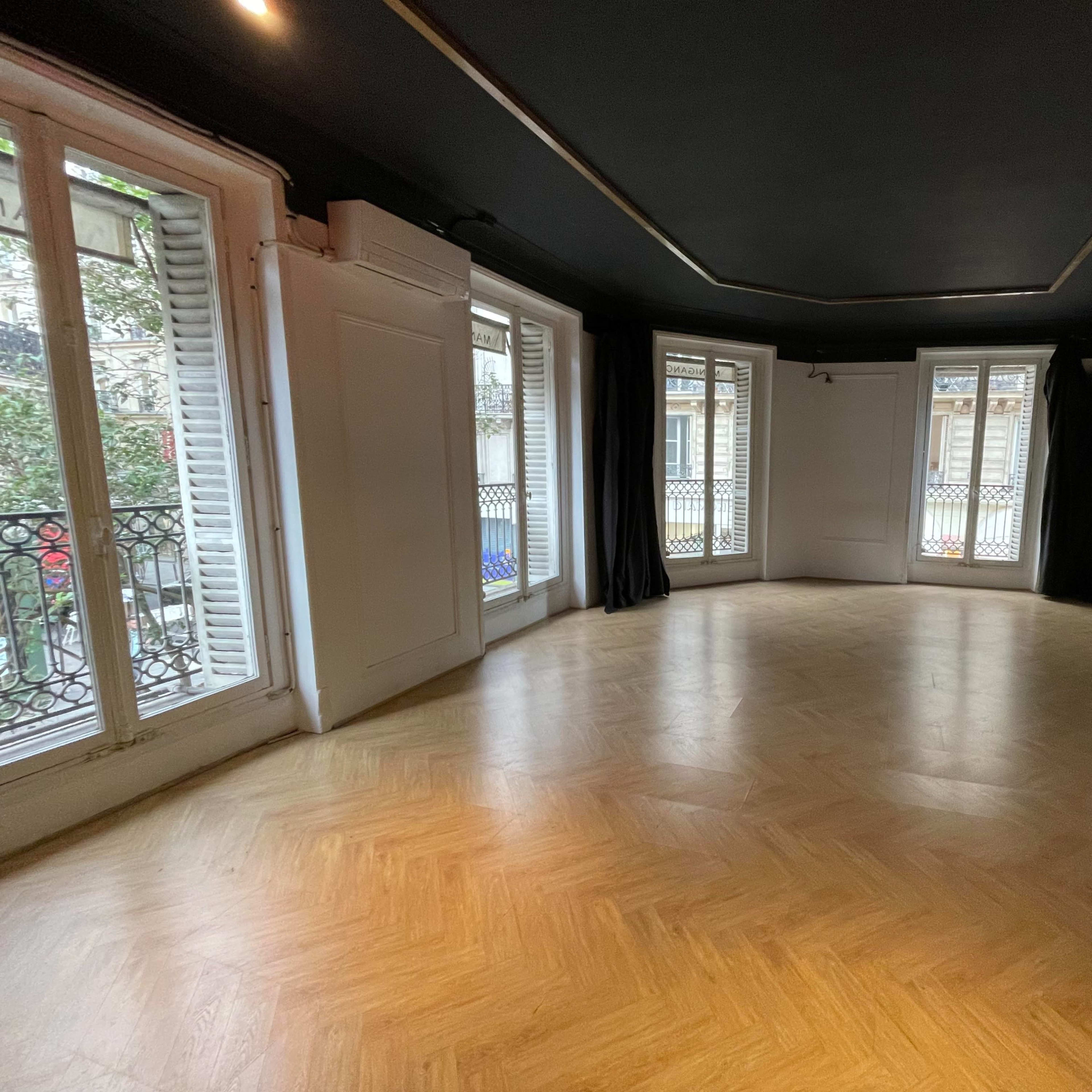 A spacious, unfurnished room with wooden flooring and large windows that open to a balcony.