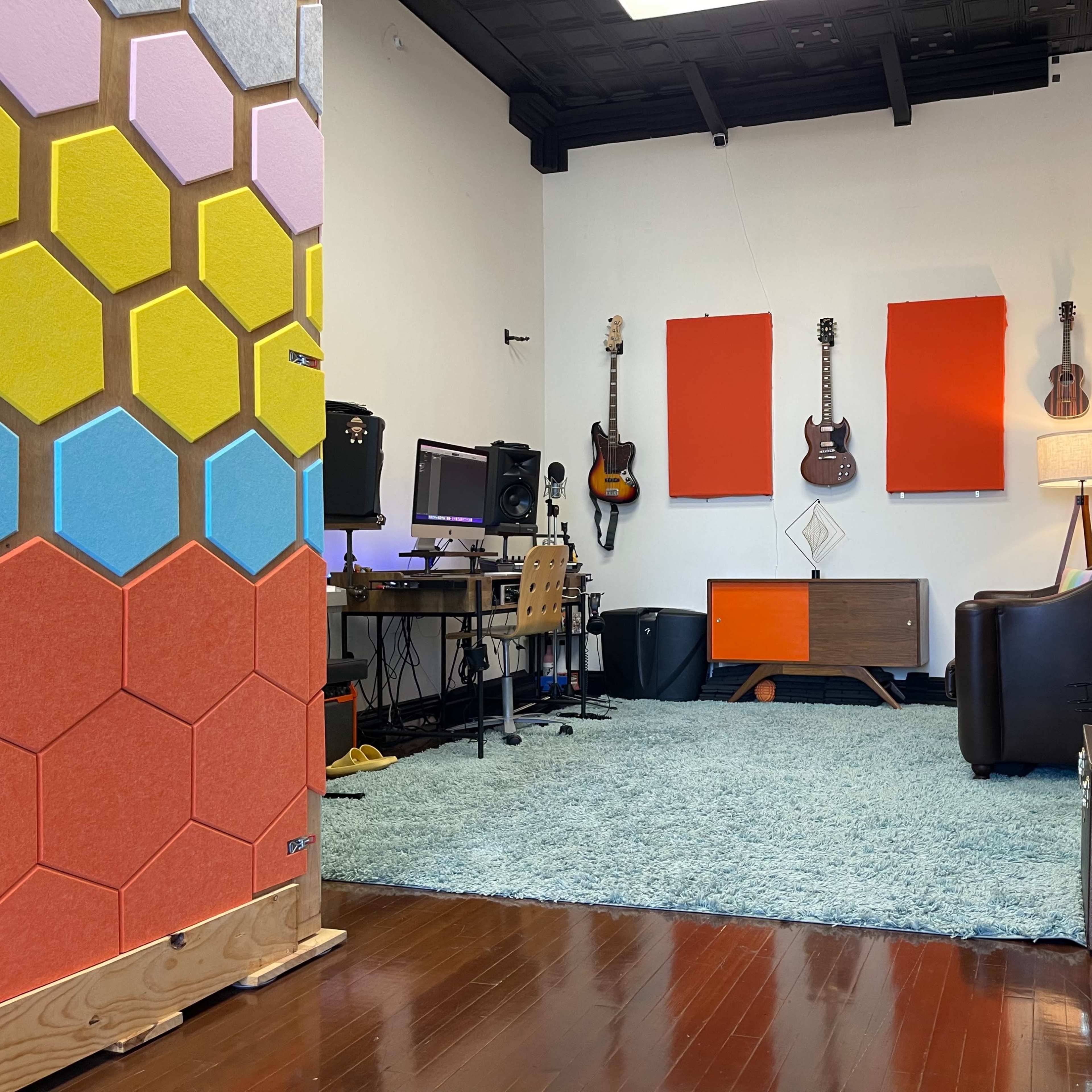 A music studio featuring guitars on the walls, a computer setup, a couch, and colorful acoustic panels.
