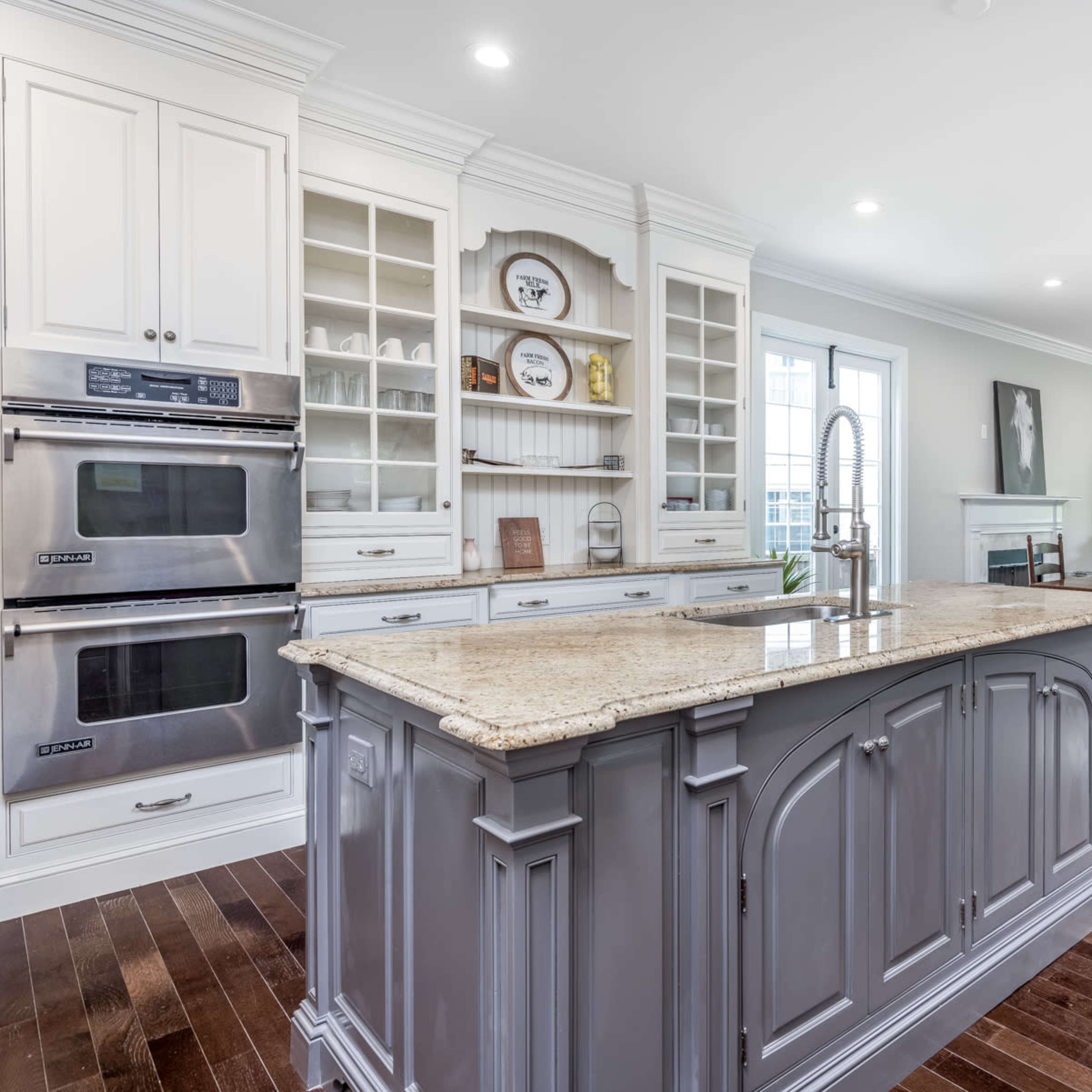 A spacious kitchen with a large island, equipped with modern appliances and wooden flooring, connected to a dining area featuring a table and chairs.