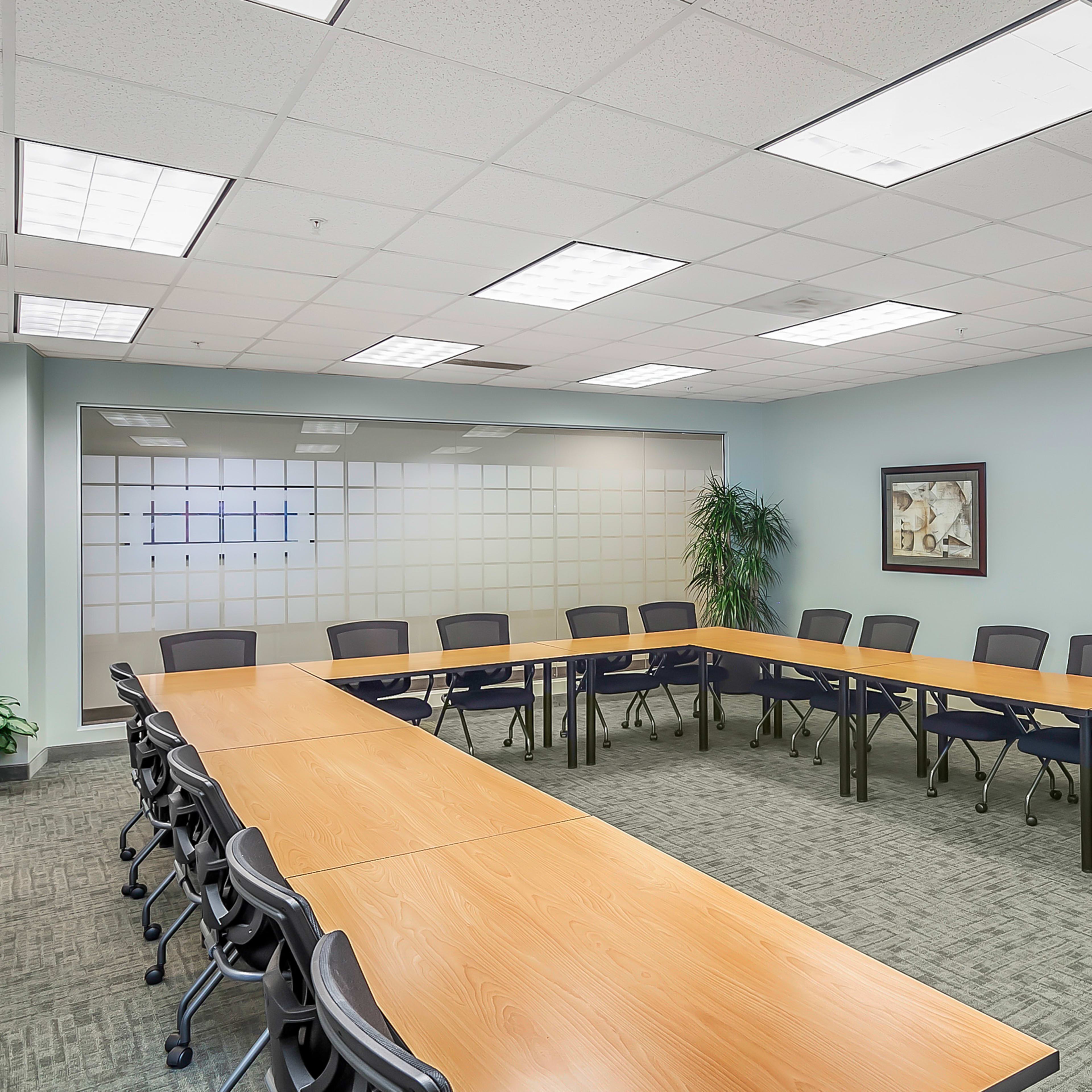 A rectangular conference room arranged with several tables and chairs, and two framed artworks on the wall.