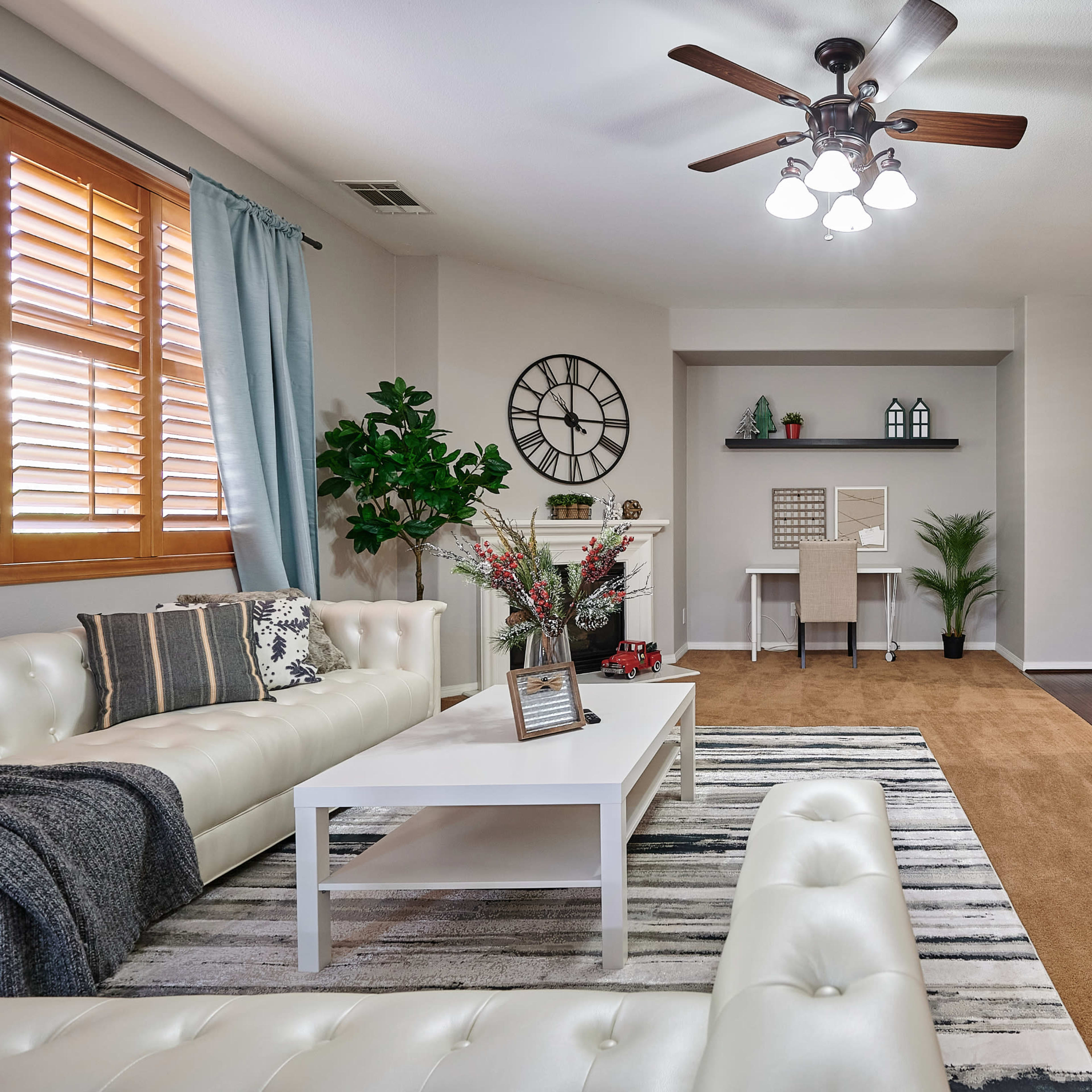 A well-decorated living room featuring a white sectional sofa, a coffee table, and a workspace with a desk against a light-colored wall.