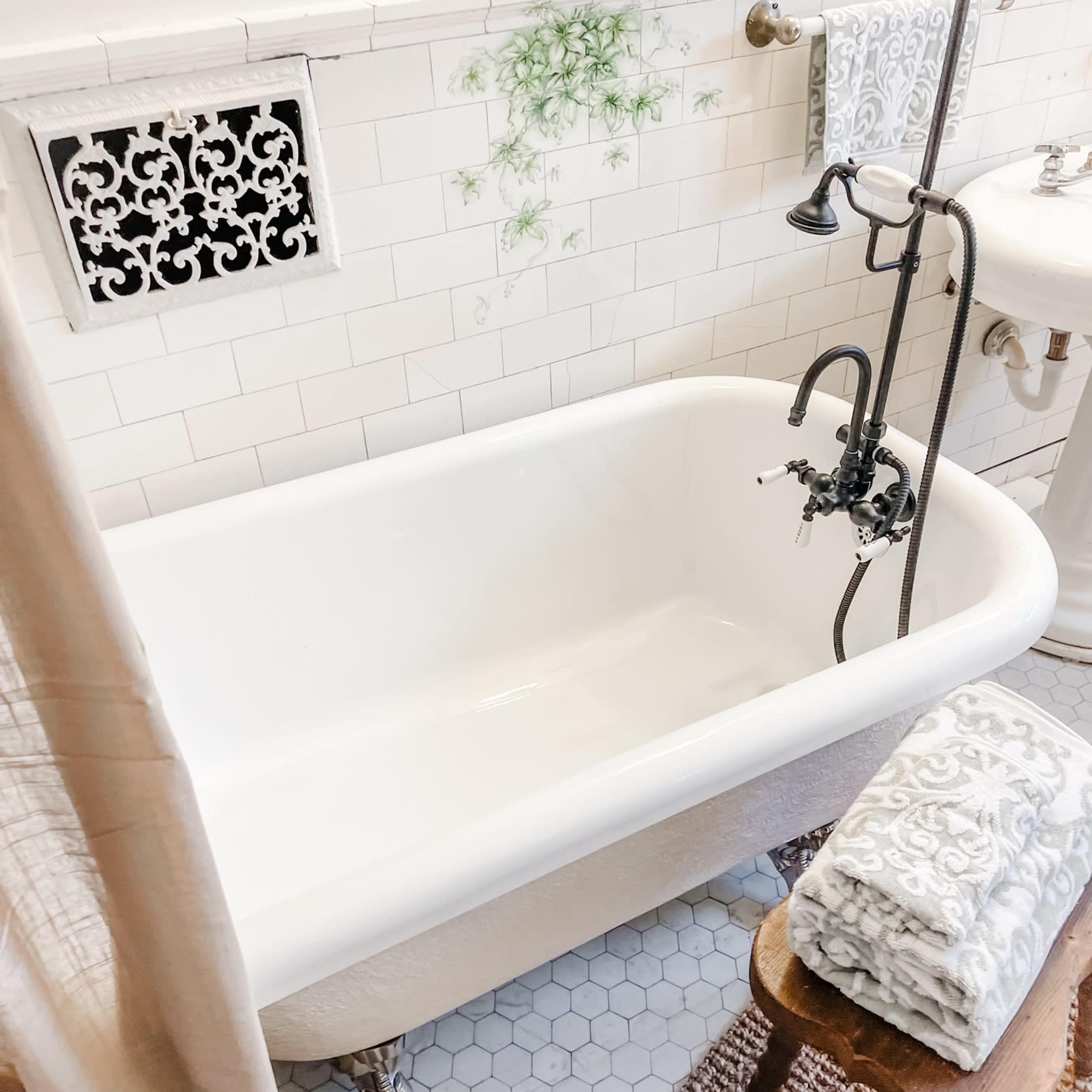 A vintage-style bathroom featuring a clawfoot bathtub, a small wooden stool, and patterned towels.